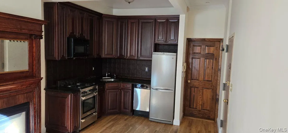 Kitchen with appliances with stainless steel finishes, backsplash, dark wood-style flooring, and dark brown cabinetry Kitchen with appliances with stainless steel finishes, backsplash, dark wood-style flooring, and dark brown cabinetry