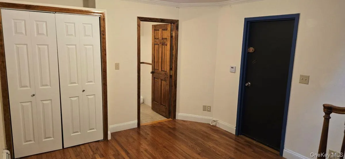 Unfurnished bedroom with dark wood-style floors, a closet, and crown molding Unfurnished bedroom with dark wood-style floors, a closet, and crown molding