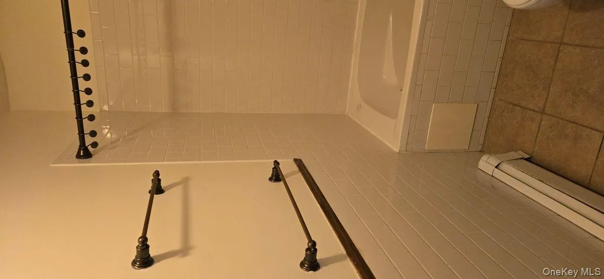 Full bathroom featuring tile walls, a baseboard radiator, tile patterned floors, tiled shower / bath combo, and a wainscoted wall Full bathroom featuring tile walls, a baseboard radiator, tile patterned floors, tiled shower / bath combo, and a wainscoted wall