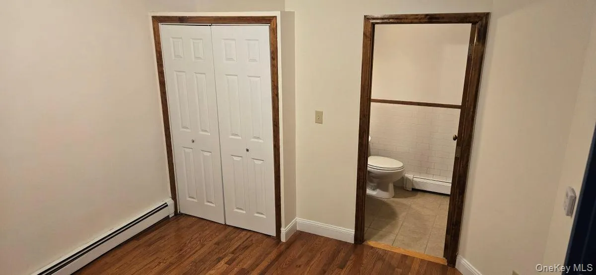 Unfurnished bedroom featuring a baseboard heating unit, a closet, and dark wood-style floors Unfurnished bedroom featuring a baseboard heating unit, a closet, and dark wood-style floors