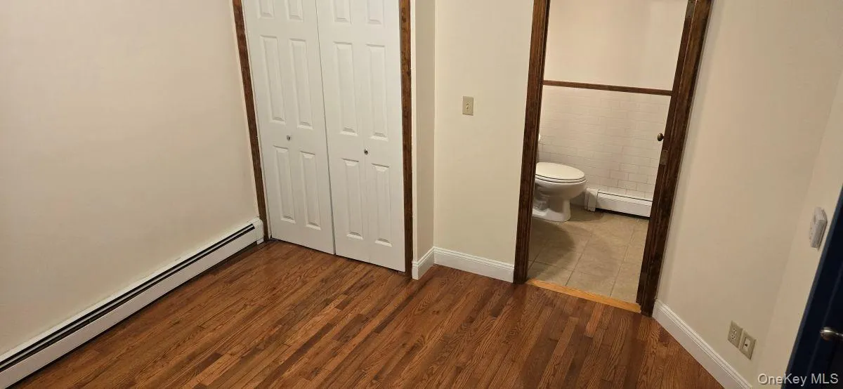 Unfurnished bedroom with a baseboard heating unit, a closet, and dark wood-style floors Unfurnished bedroom with a baseboard heating unit, a closet, and dark wood-style floors