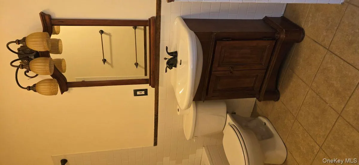 Bathroom featuring tile walls, vanity, a wainscoted wall, and light tile patterned floors Bathroom featuring tile walls, vanity, a wainscoted wall, and light tile patterned floors