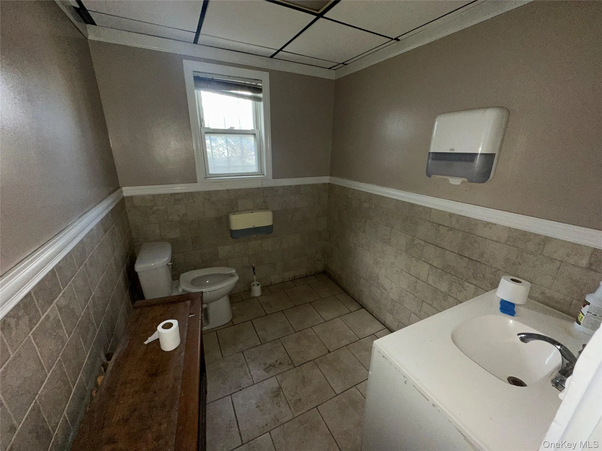 Half bath featuring a wainscoted wall, vanity, tile walls, and light tile patterned flooring Half bath featuring a wainscoted wall, vanity, tile walls, and light tile patterned flooring