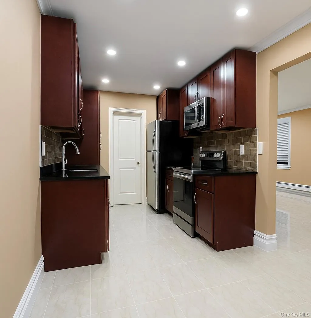 Kitchen featuring appliances with stainless steel finishes, tasteful backsplash, dark stone counters, baseboard heating, and dark brown cabinetry Kitchen featuring appliances with stainless steel finishes, tasteful backsplash, dark stone counters, baseboard heating, and dark brown cabinetry