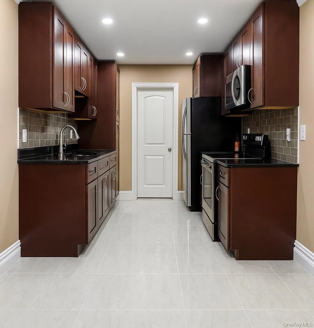 Kitchen with tasteful backsplash, appliances with stainless steel finishes, dark stone countertops, dark brown cabinetry, and recessed lighting Kitchen with tasteful backsplash, appliances with stainless steel finishes, dark stone countertops, dark brown cabinetry, and recessed lighting