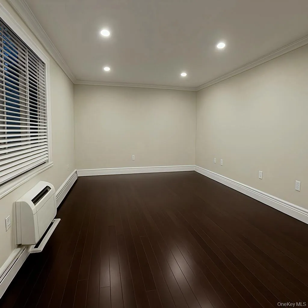 Empty room with recessed lighting, ornamental molding, dark wood-type flooring, a wall unit AC, and a baseboard radiator Empty room with recessed lighting, ornamental molding, dark wood-type flooring, a wall unit AC, and a baseboard radiator
