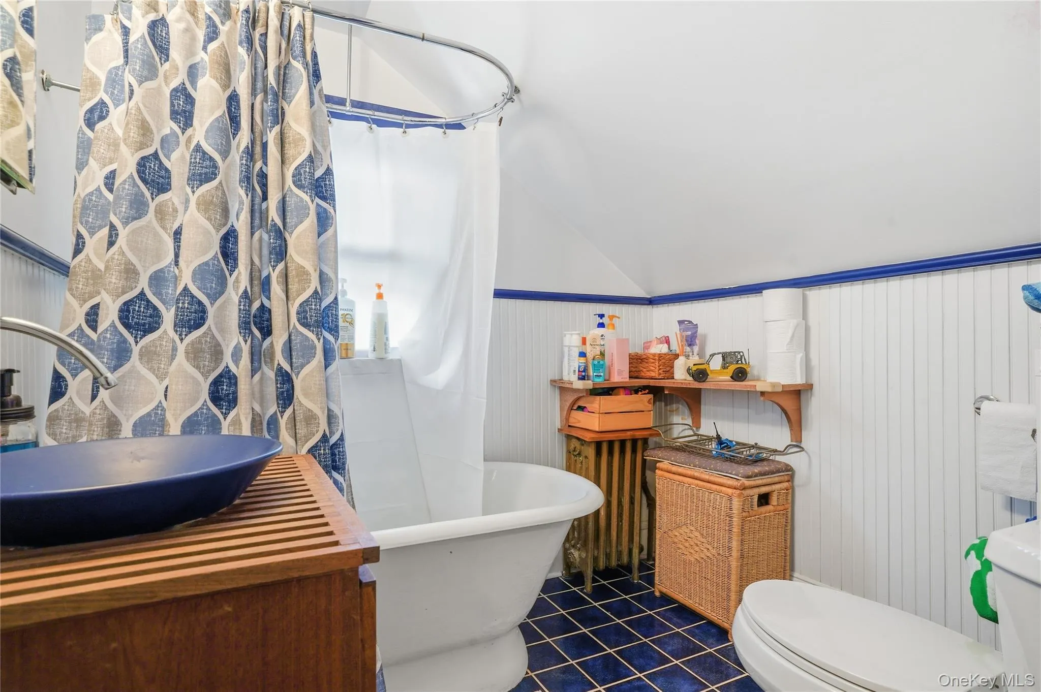 Full bath with vanity, lofted ceiling, dark tile patterned floors, wainscoting, and a combined bath / shower with freestanding tub Full bath with vanity, lofted ceiling, dark tile patterned floors, wainscoting, and a combined bath / shower with freestanding tub