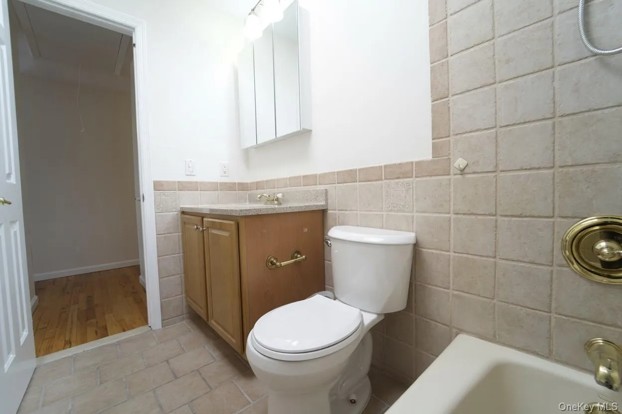 Bathroom with vanity, tile walls, wainscoting, light tile patterned floors, and shower combination Bathroom with vanity, tile walls, wainscoting, light tile patterned floors, and shower combination