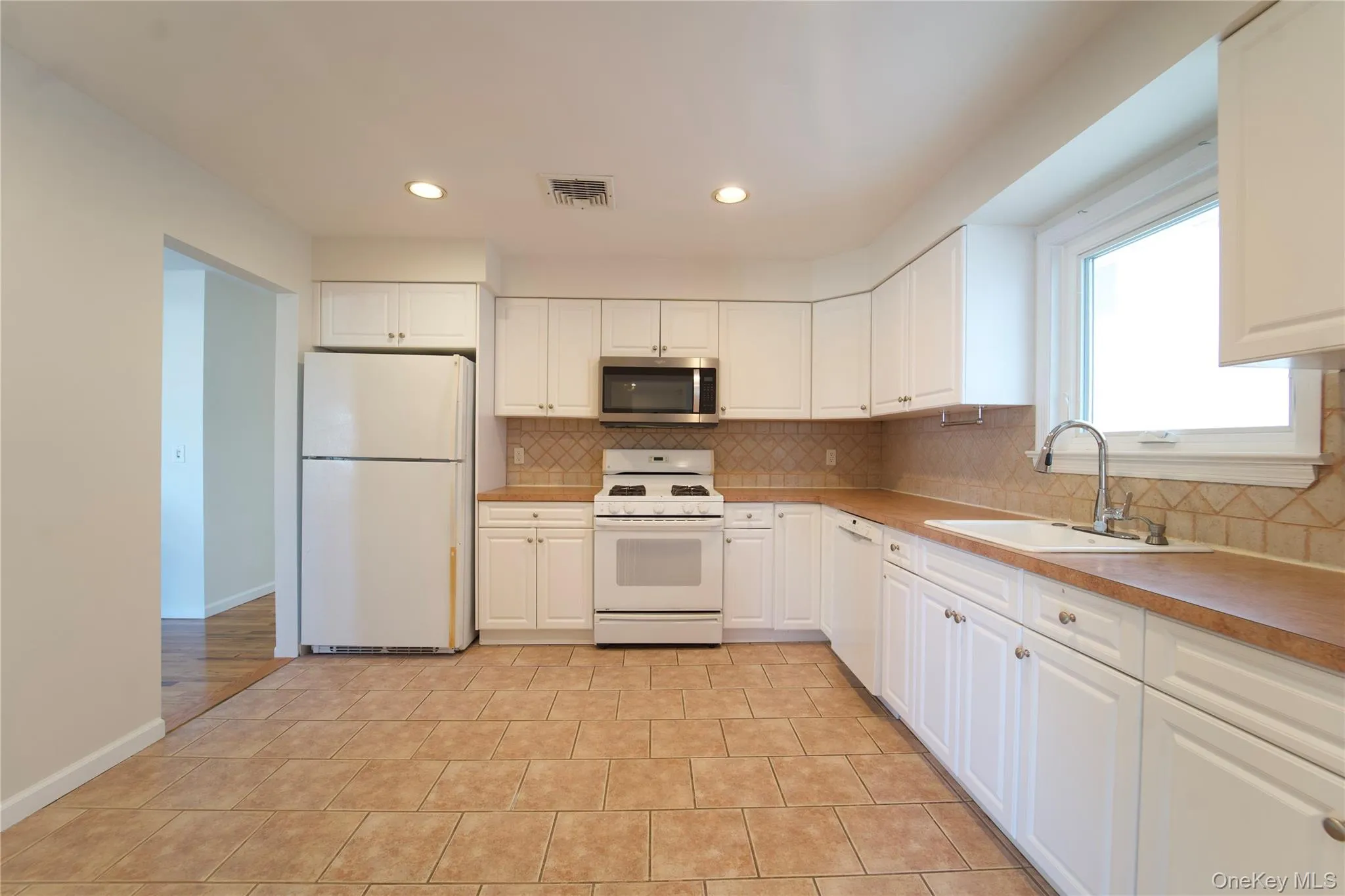 Kitchen featuring white appliances, light countertops, white cabinetry, backsplash, and recessed lighting Kitchen featuring white appliances, light countertops, white cabinetry, backsplash, and recessed lighting