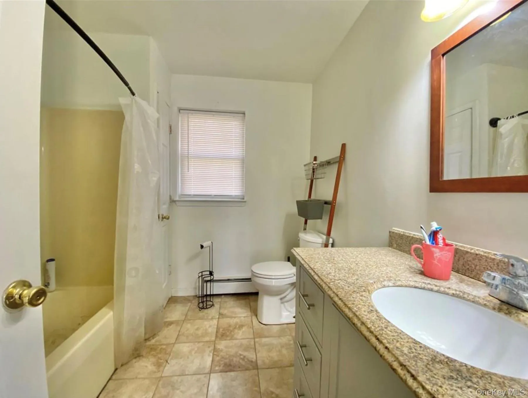 Full bath featuring shower / bath combination with curtain, vanity, baseboard heating, and light tile patterned floors Full bath featuring shower / bath combination with curtain, vanity, baseboard heating, and light tile patterned floors