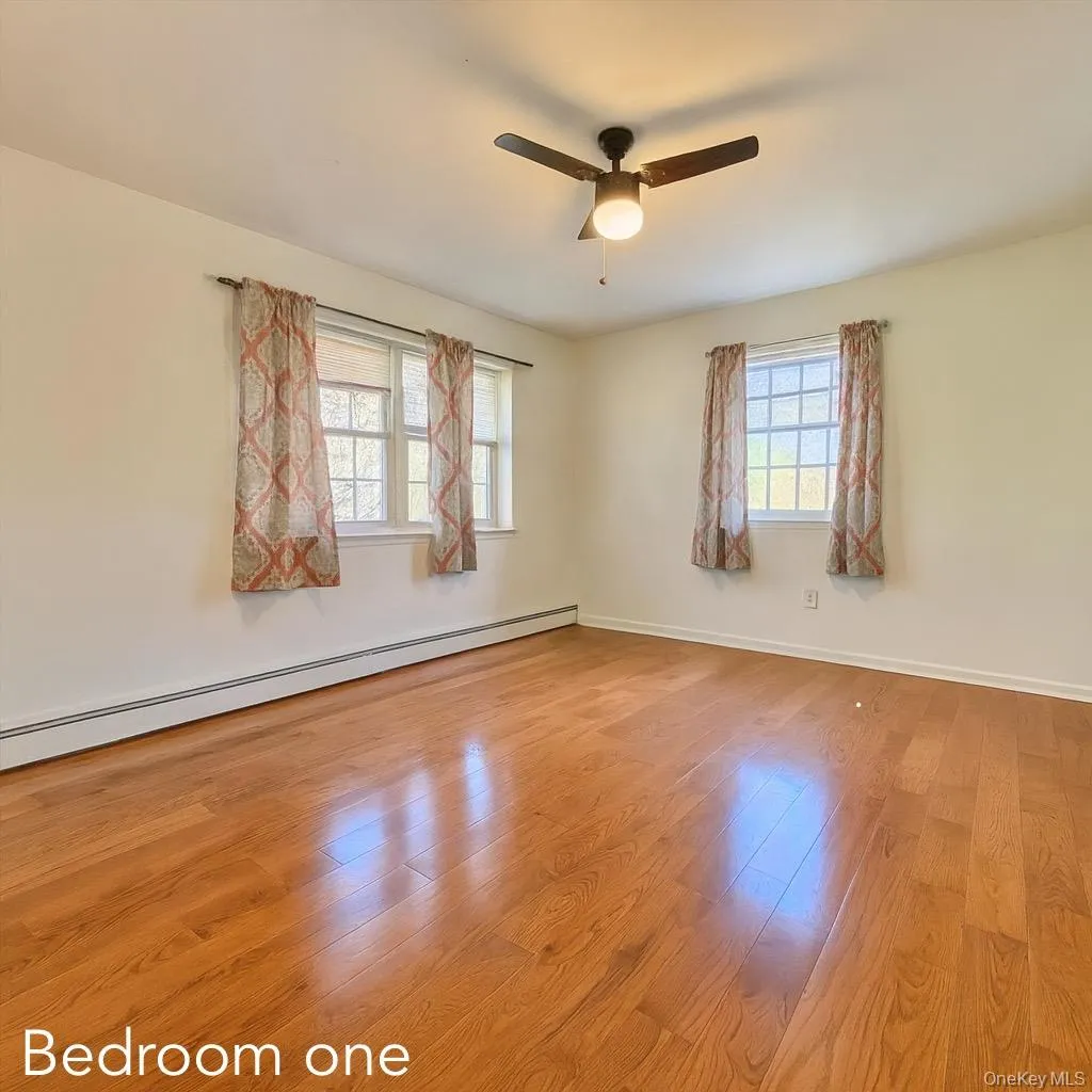 Empty room with a baseboard heating unit, light wood-style flooring, and ceiling fan Empty room with a baseboard heating unit, light wood-style flooring, and ceiling fan