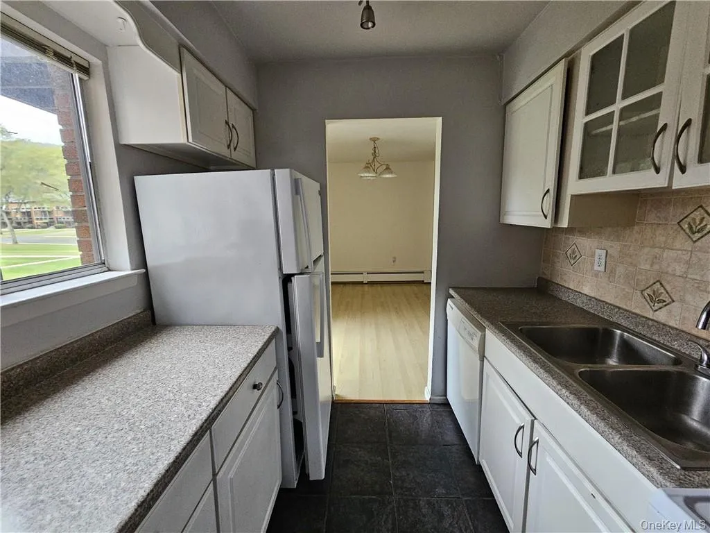 Kitchen featuring white cabinets, dark tile patterned floors, sink, white appliances, and a baseboard heating unit Kitchen featuring white cabinets, dark tile patterned floors, sink, white appliances, and a baseboard heating unit