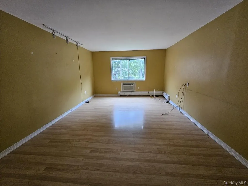 Empty room with wood-type flooring, a wall mounted air conditioner, a baseboard heating unit, and rail lighting Empty room with wood-type flooring, a wall mounted air conditioner, a baseboard heating unit, and rail lighting