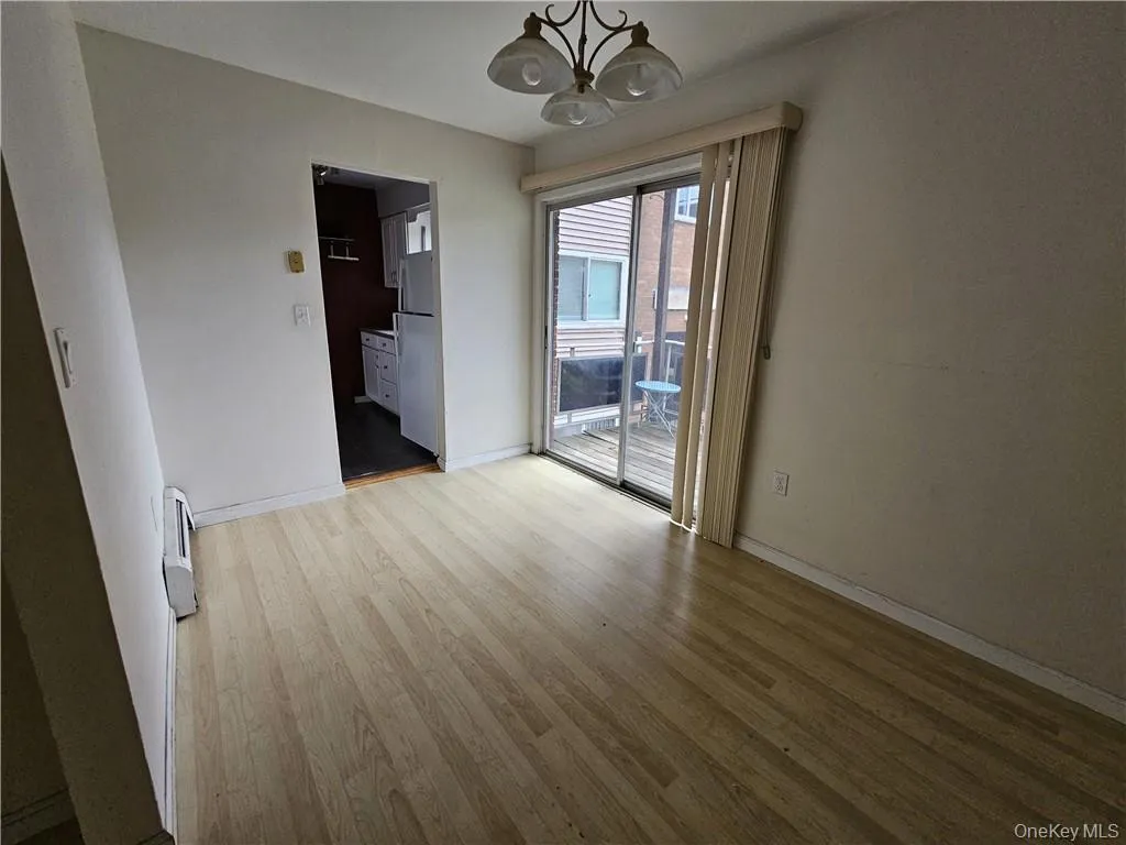 Unfurnished room featuring a notable chandelier, light wood-type flooring, and a baseboard heating unit Unfurnished room featuring a notable chandelier, light wood-type flooring, and a baseboard heating unit