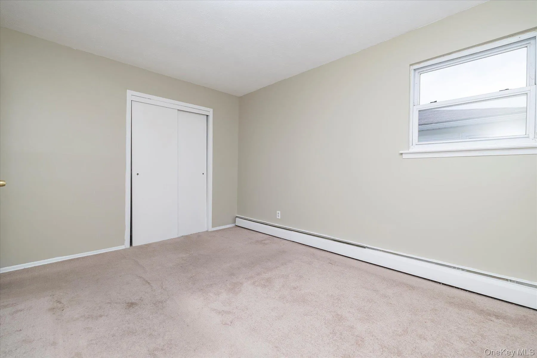 Unfurnished bedroom with a baseboard radiator, a closet, and light carpet Unfurnished bedroom with a baseboard radiator, a closet, and light carpet