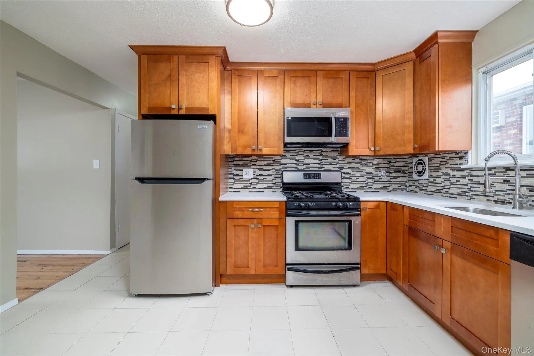 Kitchen with stainless steel appliances, brown cabinets, light stone countertops, and tasteful backsplash Kitchen with stainless steel appliances, brown cabinets, light stone countertops, and tasteful backsplash