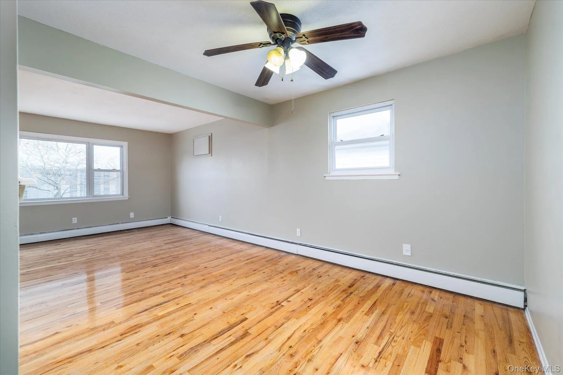 Empty room with a baseboard heating unit, light wood finished floors, and plenty of natural light Empty room with a baseboard heating unit, light wood finished floors, and plenty of natural light