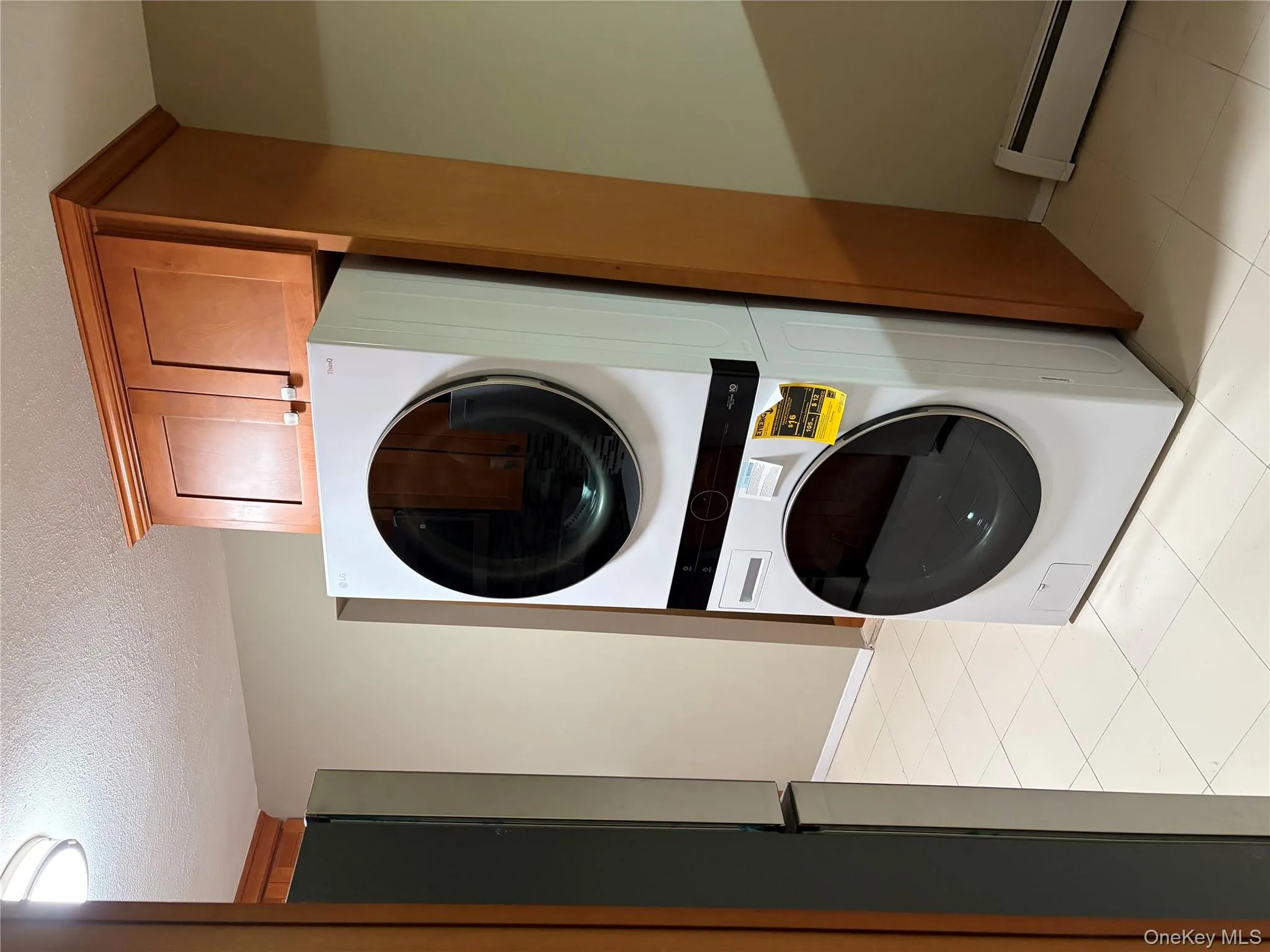 Laundry room featuring a baseboard heating unit, stacked washer / dryer, a textured ceiling, and light tile patterned flooring Laundry room featuring a baseboard heating unit, stacked washer / dryer, a textured ceiling, and light tile patterned flooring