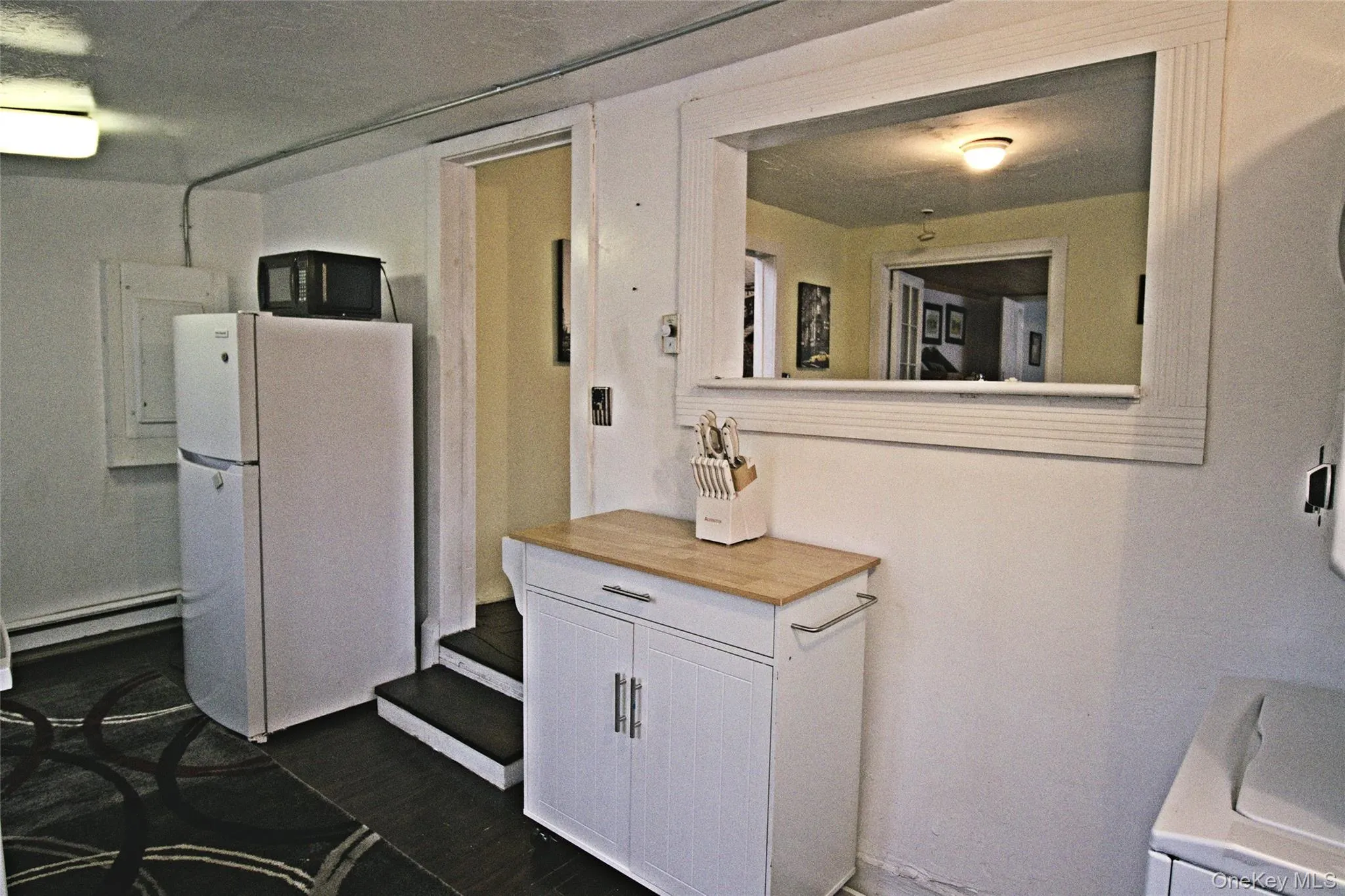 Kitchen with white cabinetry, freestanding refrigerator, a baseboard heating unit, black microwave, and wood counters Kitchen with white cabinetry, freestanding refrigerator, a baseboard heating unit, black microwave, and wood counters