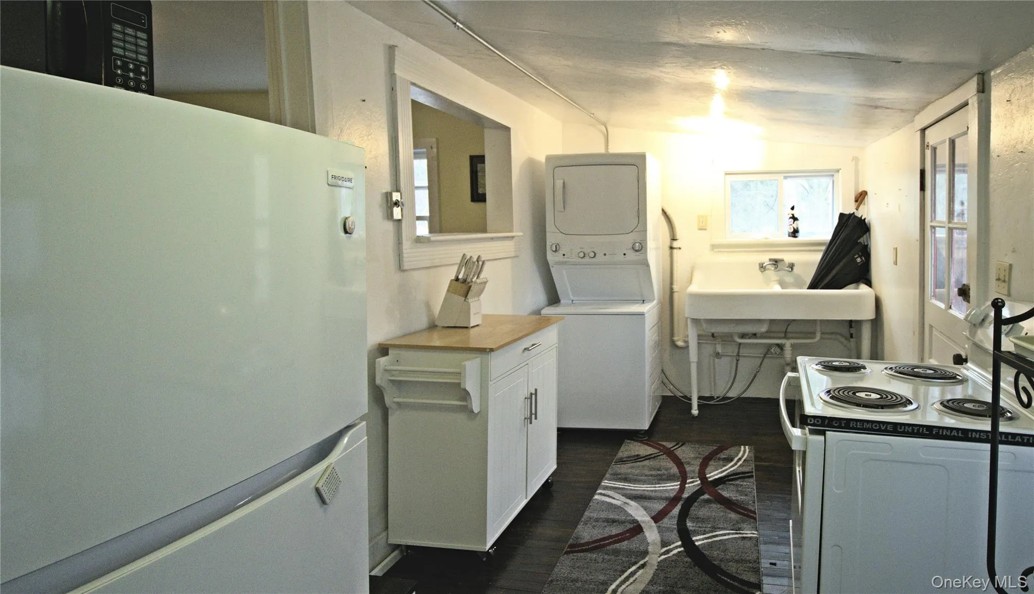 Kitchen with freestanding refrigerator, range with electric cooktop, dark wood-style floors, white cabinets, and estacked washer and dryer Kitchen with freestanding refrigerator, range with electric cooktop, dark wood-style floors, white cabinets, and estacked washer and dryer