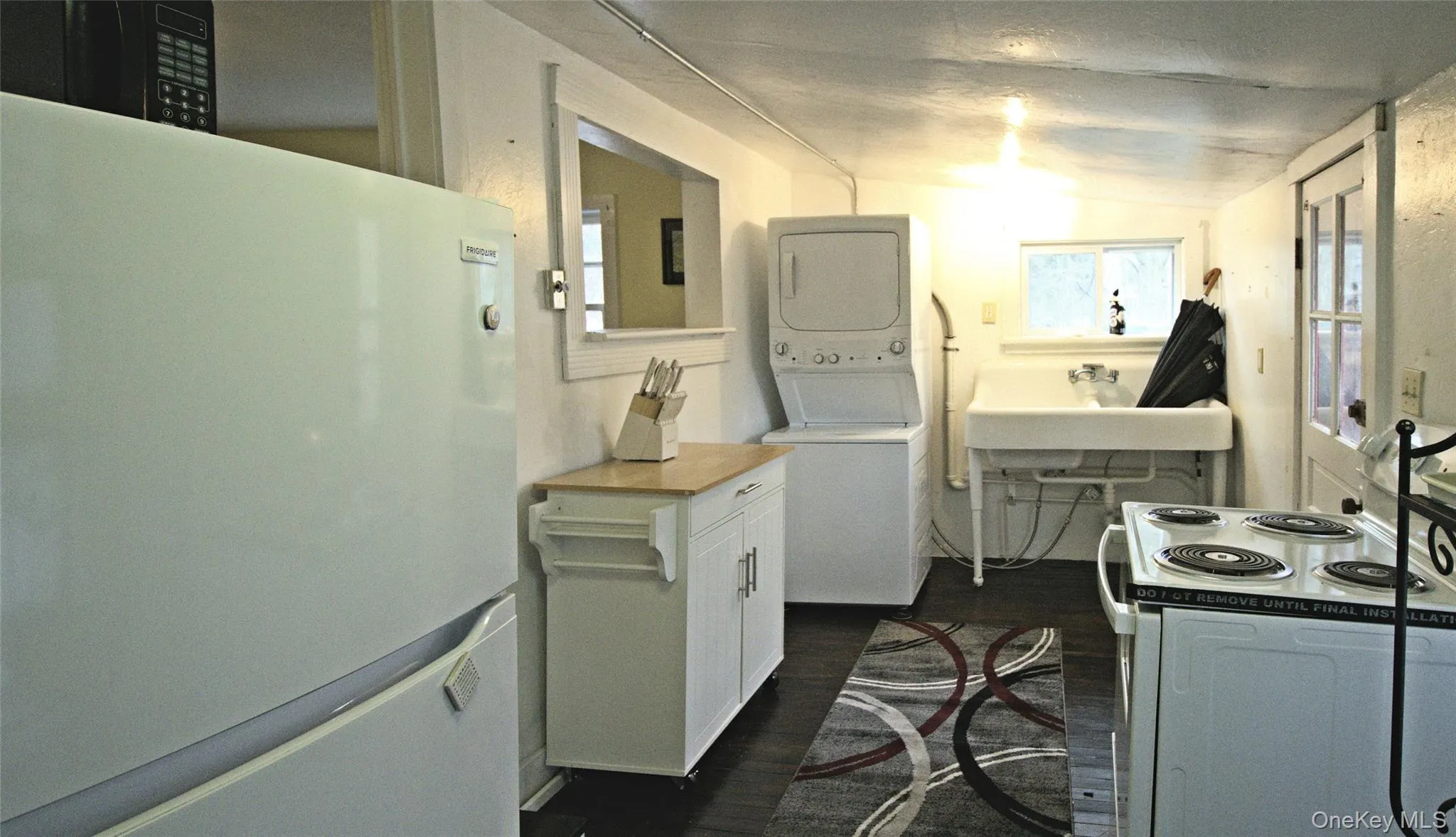 Kitchen featuring freestanding refrigerator, electric range oven, dark wood-style flooring, white cabinets, and stacked washer / drying machine Kitchen featuring freestanding refrigerator, electric range oven, dark wood-style flooring, white cabinets, and stacked washer / drying machine