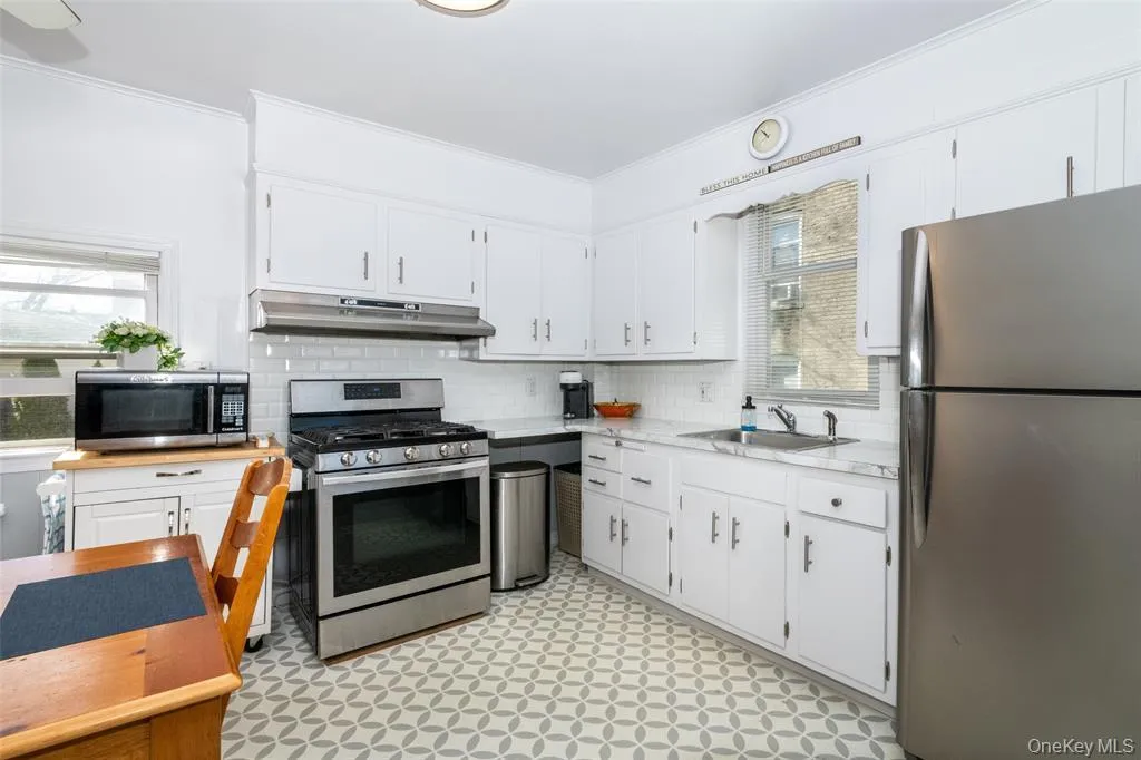 Kitchen with stainless steel appliances, light floors, white cabinetry, decorative backsplash, and ornamental molding Kitchen with stainless steel appliances, light floors, white cabinetry, decorative backsplash, and ornamental molding