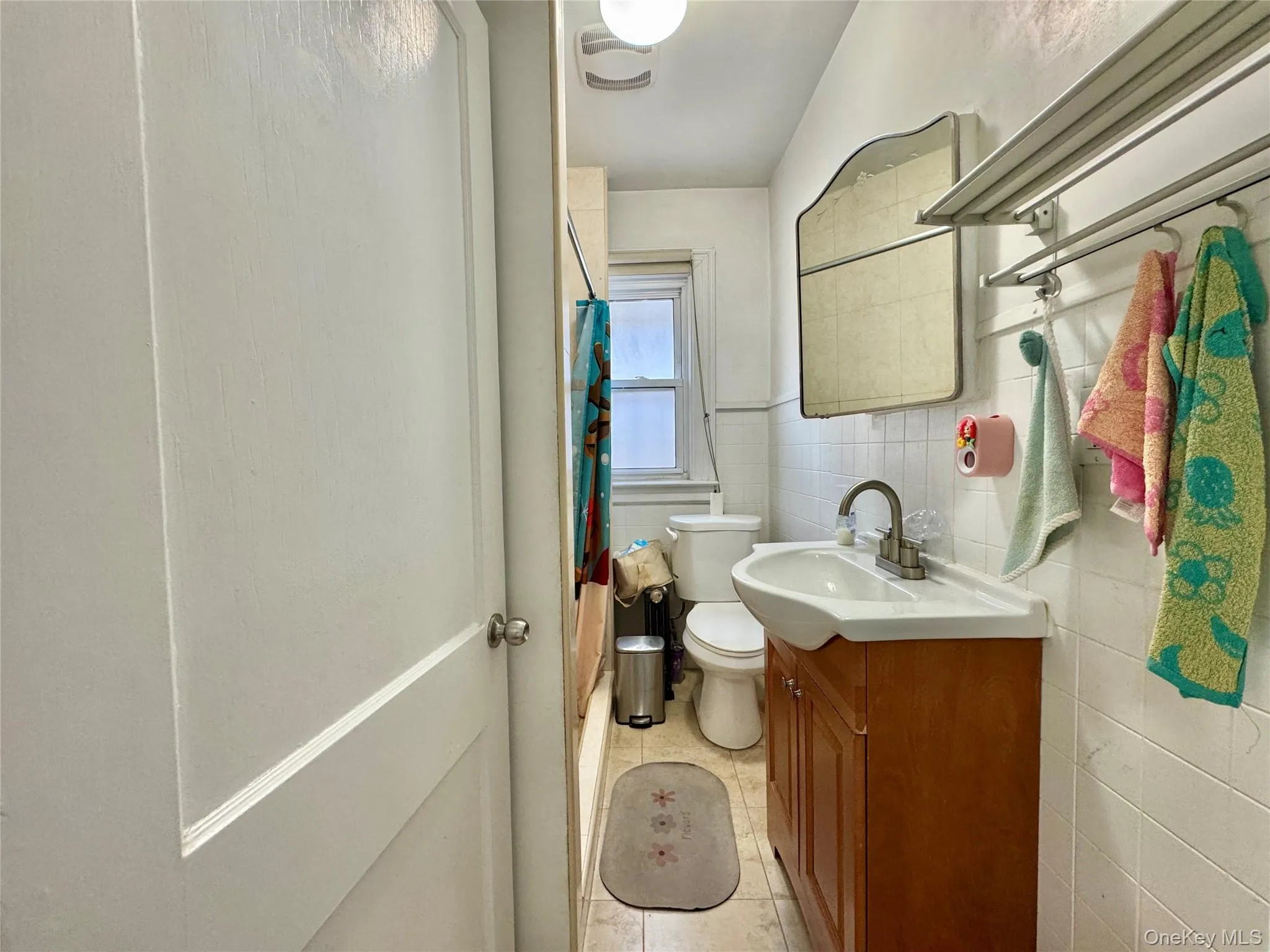 Full bathroom with vanity, a shower with curtain, tile walls, light tile patterned floors, and a wainscoted wall Full bathroom with vanity, a shower with curtain, tile walls, light tile patterned floors, and a wainscoted wall
