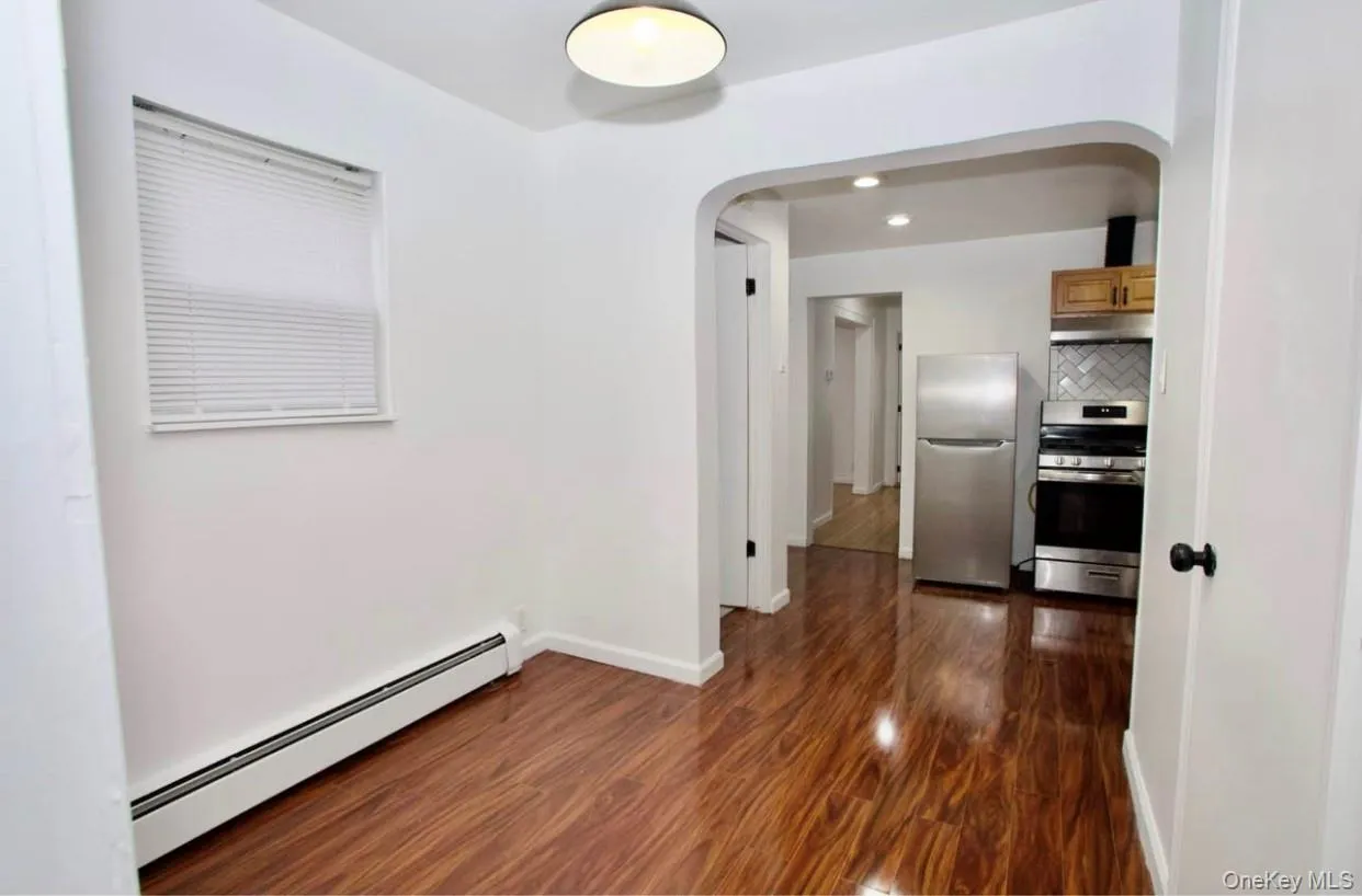 Spare room featuring baseboard heating, arched walkways, dark wood-style flooring, and recessed lighting Spare room featuring baseboard heating, arched walkways, dark wood-style flooring, and recessed lighting