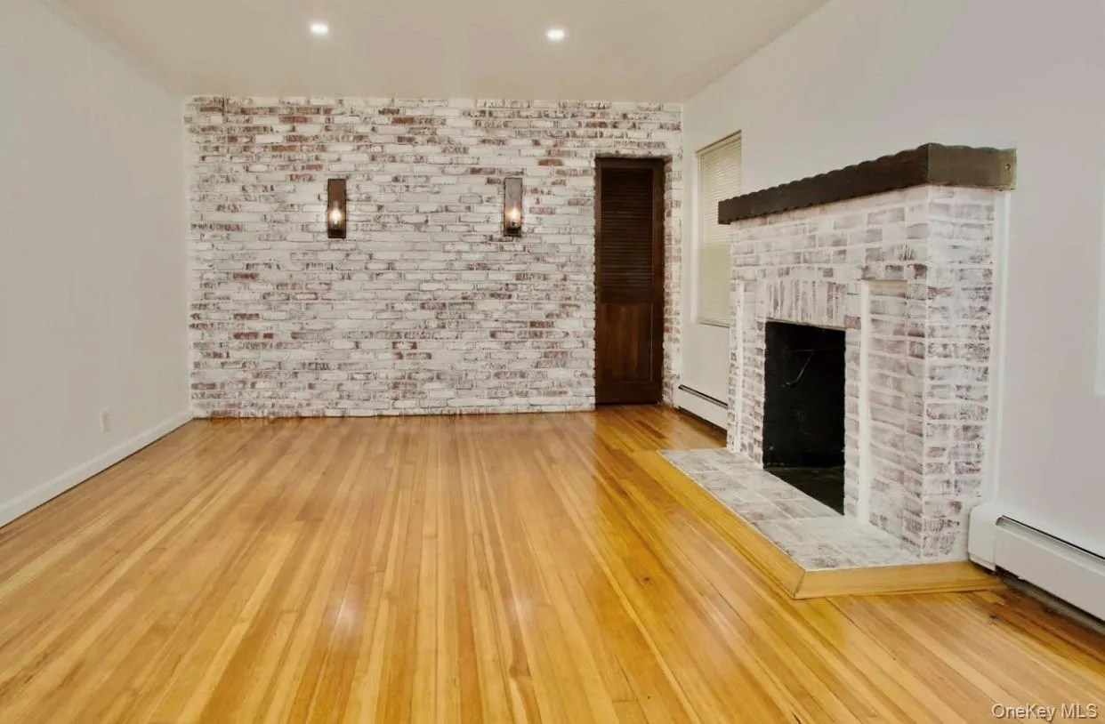 Unfurnished living room featuring a fireplace, a baseboard heating unit, light wood finished floors, recessed lighting, and brick wall Unfurnished living room featuring a fireplace, a baseboard heating unit, light wood finished floors, recessed lighting, and brick wall