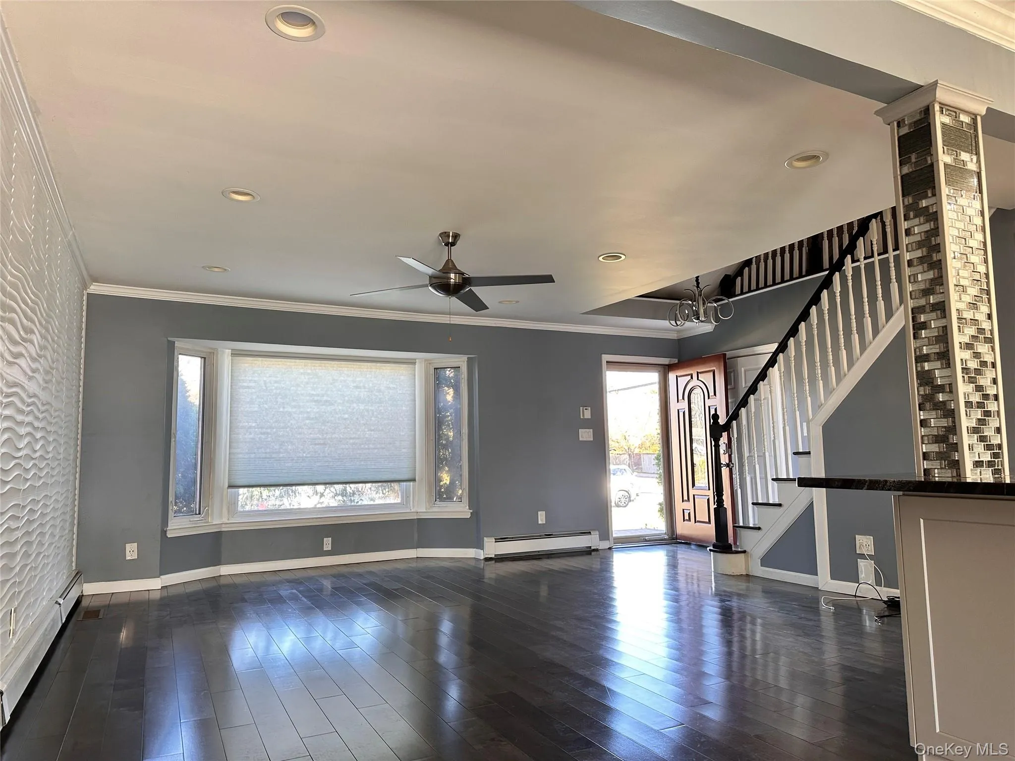 Unfurnished living room with crown molding, dark wood-type flooring, stairway, a baseboard heating unit, and baseboard heating Unfurnished living room with crown molding, dark wood-type flooring, stairway, a baseboard heating unit, and baseboard heating
