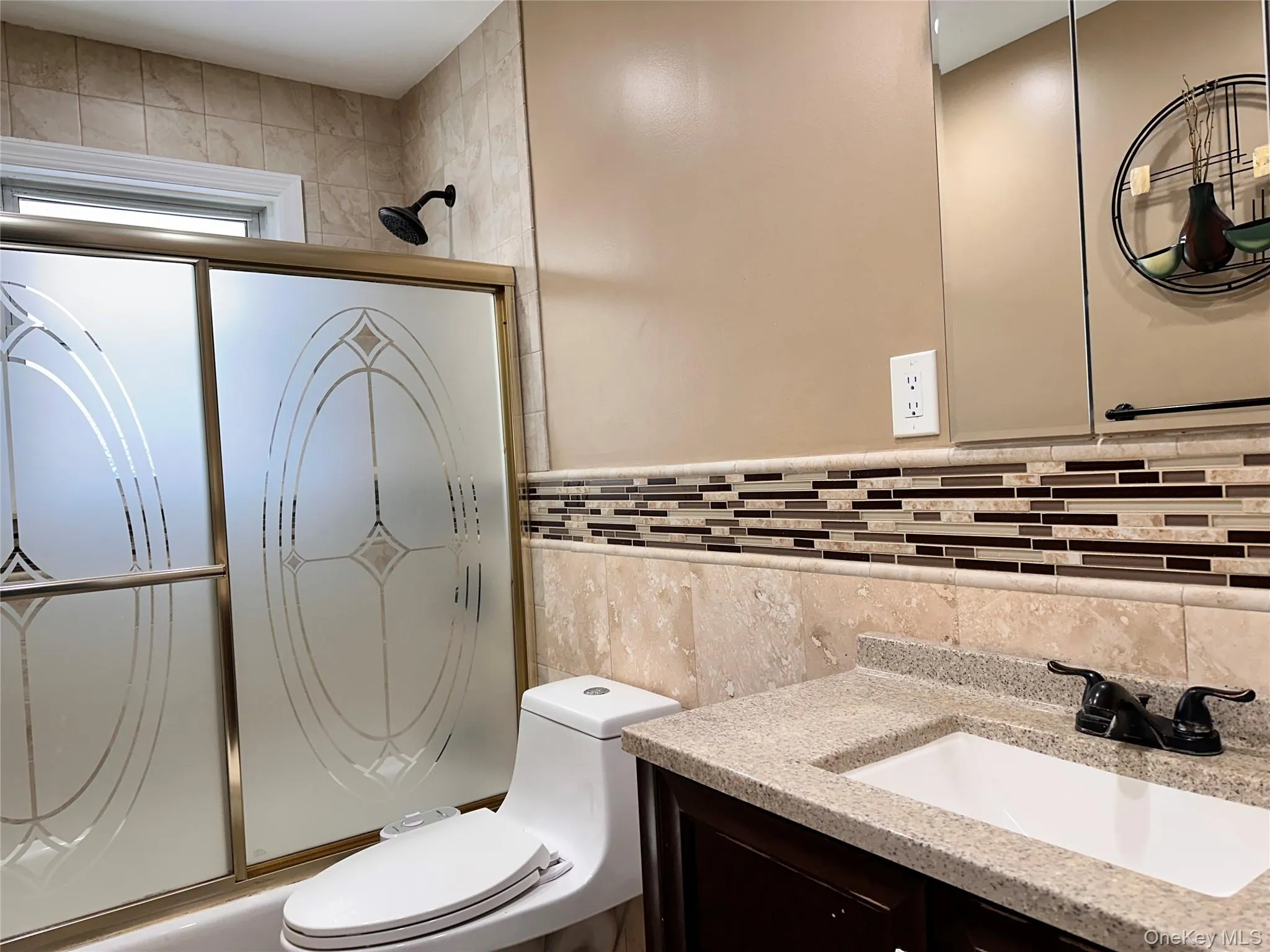 Bathroom with vanity, tile walls, and bath / shower combo with glass door Bathroom with vanity, tile walls, and bath / shower combo with glass door
