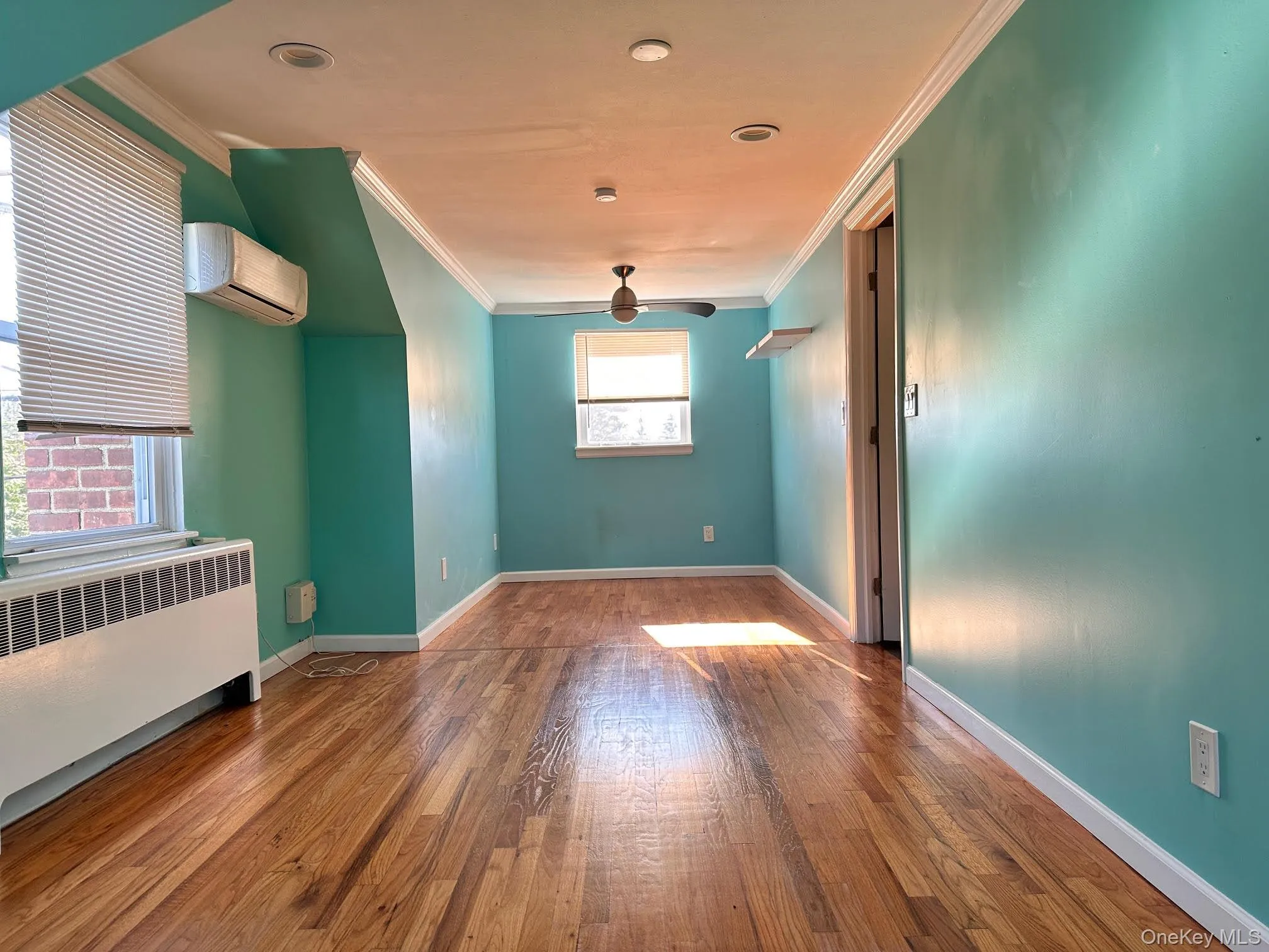 Spare room with radiator, hardwood / wood-style flooring, crown molding, and a wall mounted AC Spare room with radiator, hardwood / wood-style flooring, crown molding, and a wall mounted AC