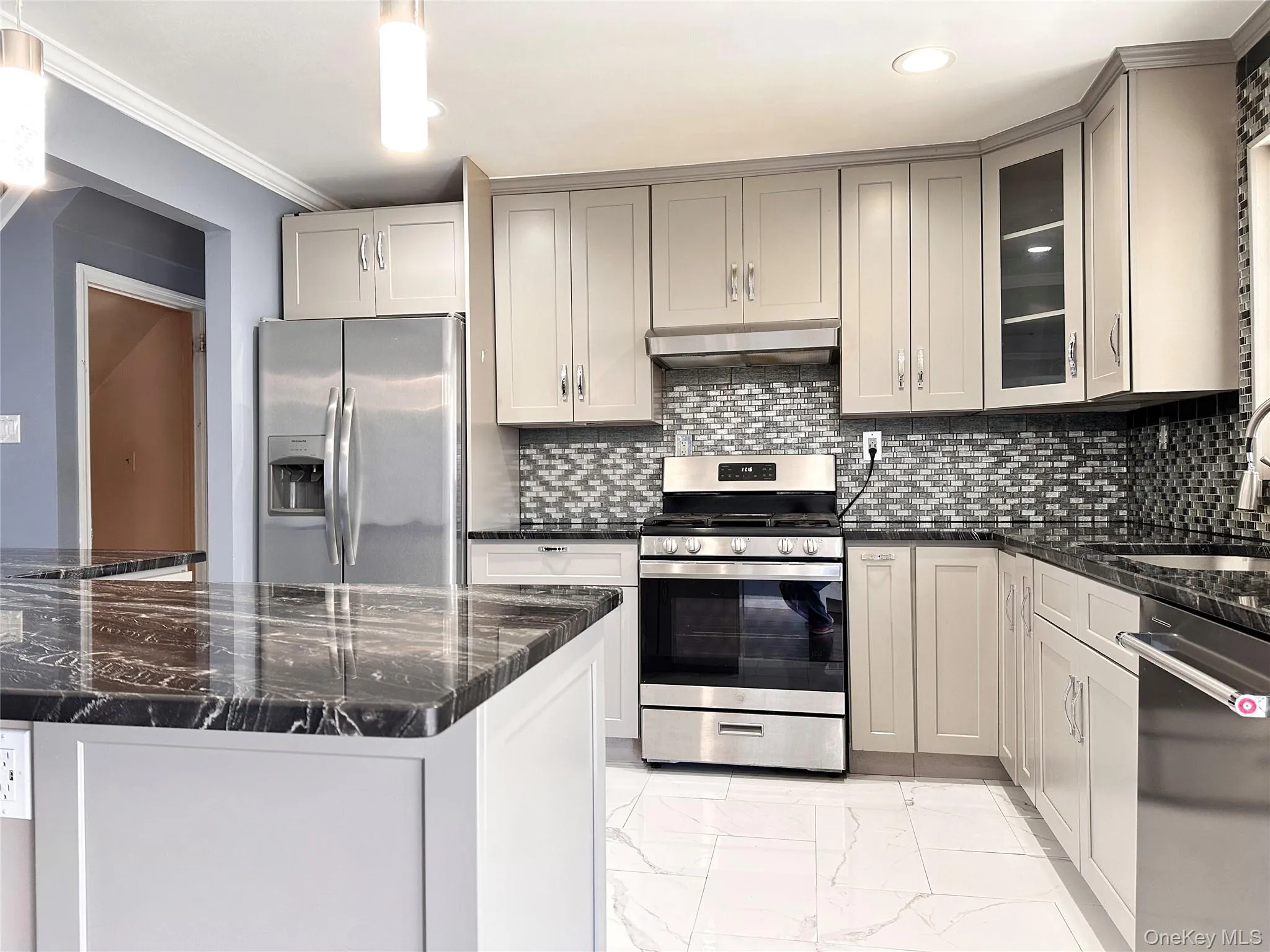 Kitchen featuring dark stone counters, appliances with stainless steel finishes, light marble finish flooring, ornamental molding, and glass insert cabinets Kitchen featuring dark stone counters, appliances with stainless steel finishes, light marble finish flooring, ornamental molding, and glass insert cabinets