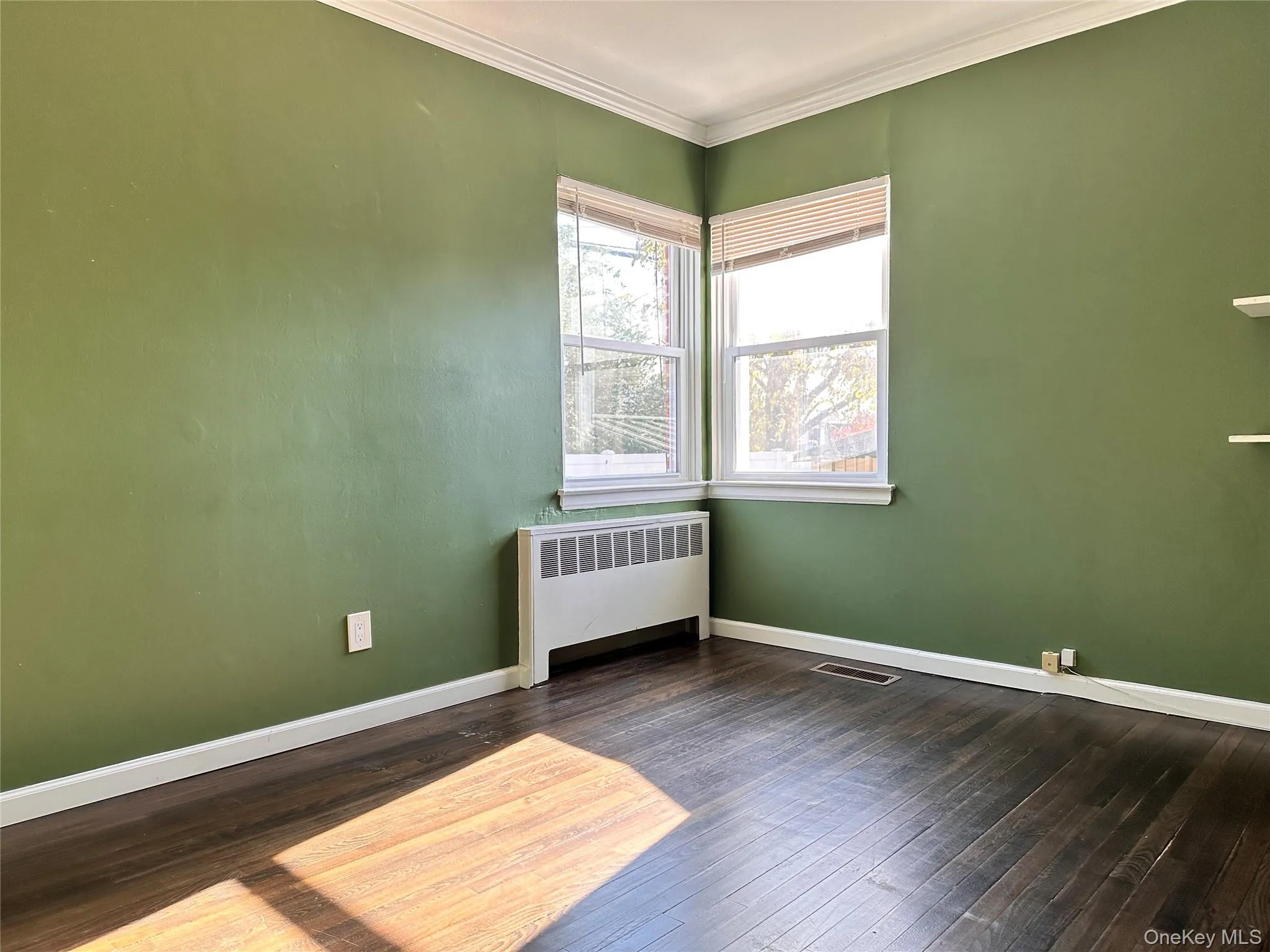 Empty room featuring radiator, dark wood-type flooring, and ornamental molding Empty room featuring radiator, dark wood-type flooring, and ornamental molding