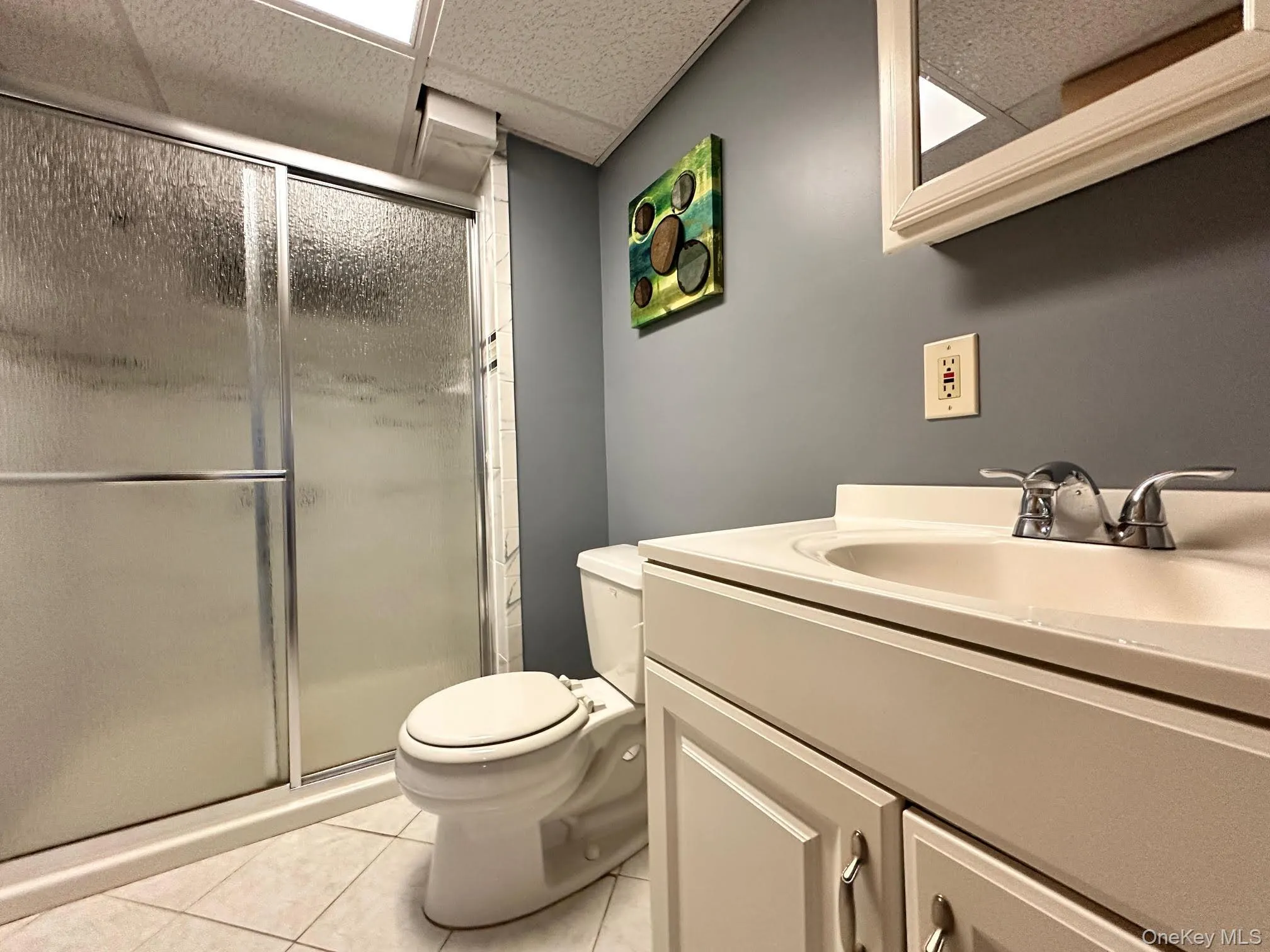 Full bathroom with vanity, a stall shower, light tile patterned floors, and a drop ceiling Full bathroom with vanity, a stall shower, light tile patterned floors, and a drop ceiling