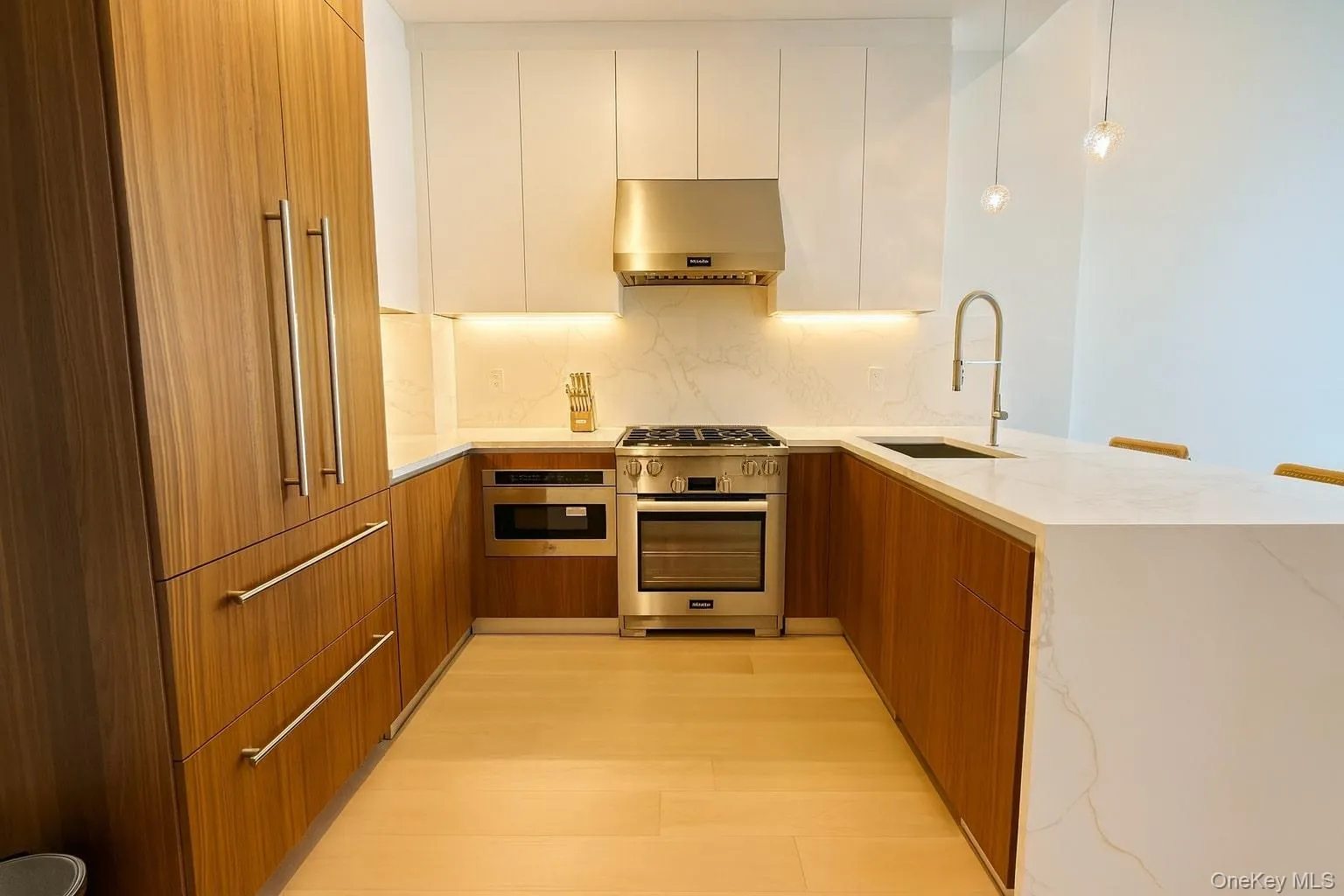 Kitchen featuring modern cabinets, a peninsula, light stone countertops, and appliances with stainless steel finishes Kitchen featuring modern cabinets, a peninsula, light stone countertops, and appliances with stainless steel finishes