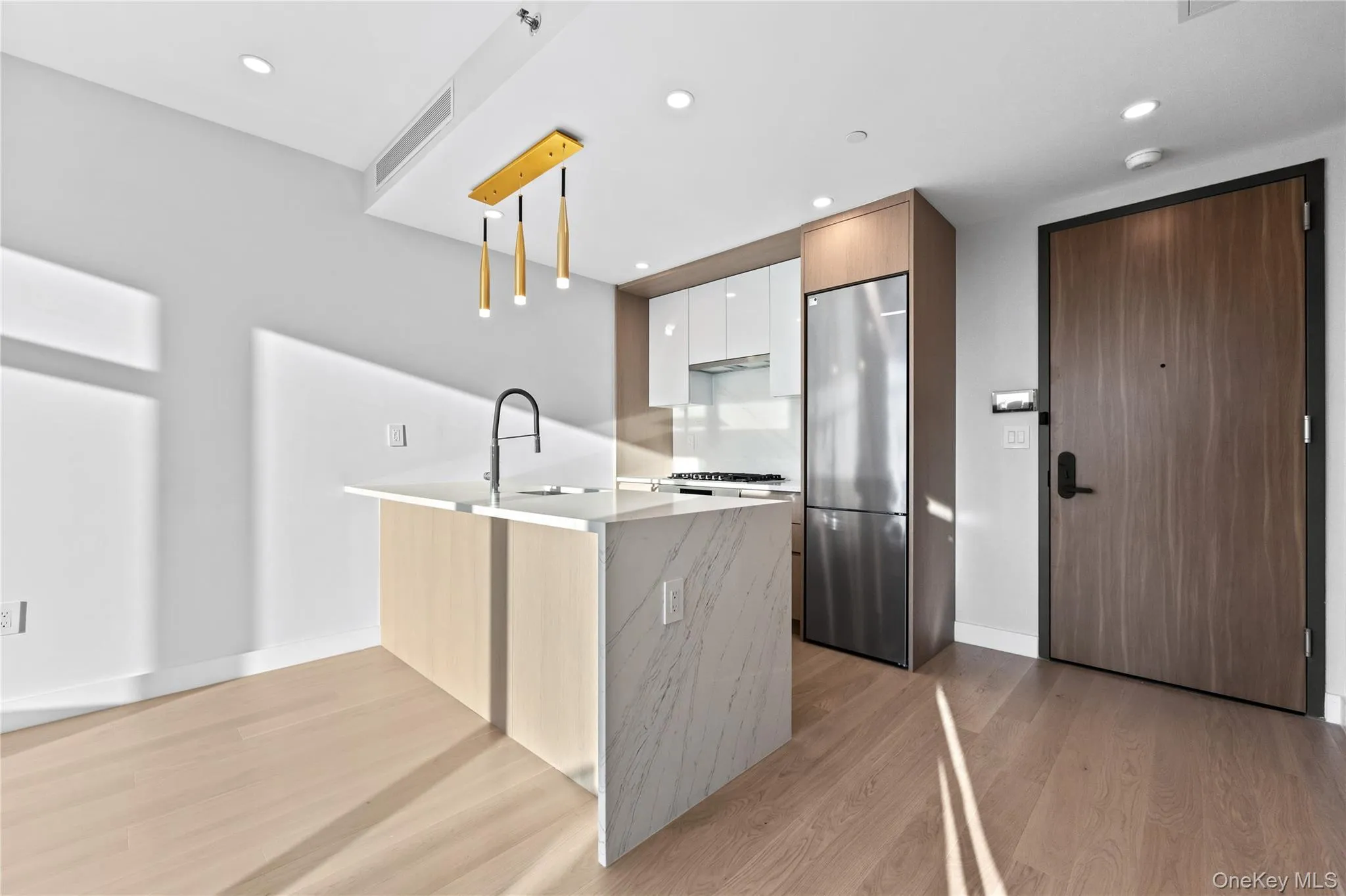 Kitchen with modern cabinets, a peninsula, light stone countertops, light wood-type flooring, and white cabinets Kitchen with modern cabinets, a peninsula, light stone countertops, light wood-type flooring, and white cabinets