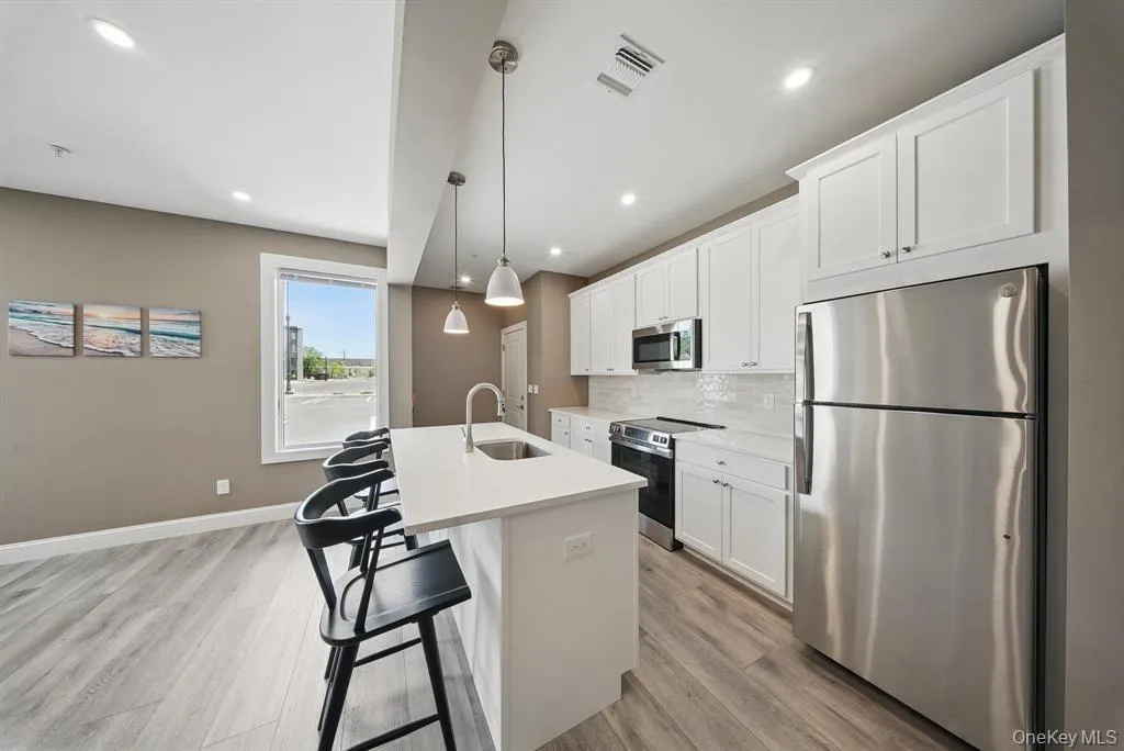 Kitchen with appliances with stainless steel finishes, a kitchen breakfast bar, white cabinetry, a center island with sink, and recessed lighting Kitchen with appliances with stainless steel finishes, a kitchen breakfast bar, white cabinetry, a center island with sink, and recessed lighting