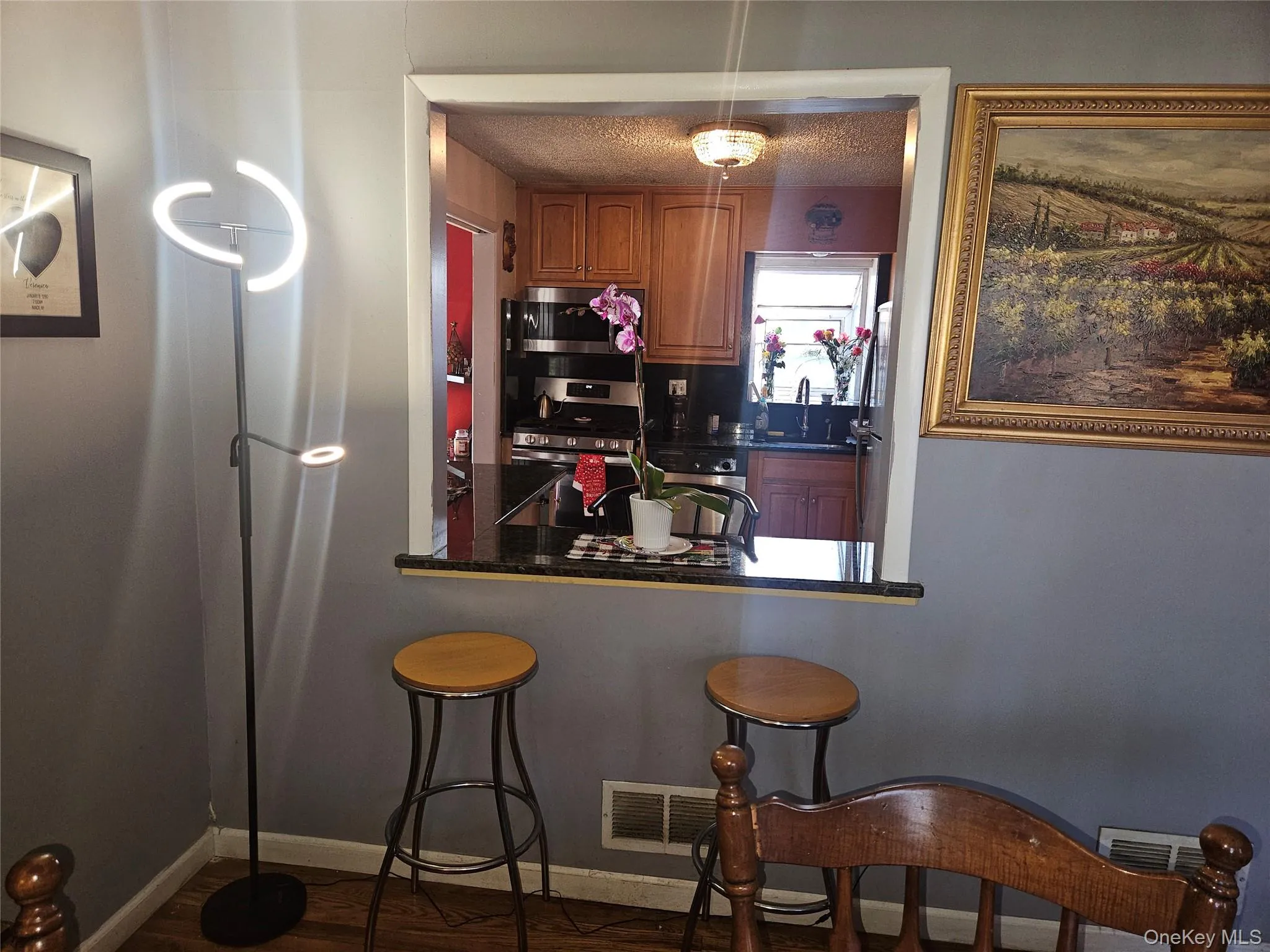 Kitchen with brown cabinets, stainless steel appliances, a kitchen bar, dark wood finished floors, and a textured ceiling Kitchen with brown cabinets, stainless steel appliances, a kitchen bar, dark wood finished floors, and a textured ceiling