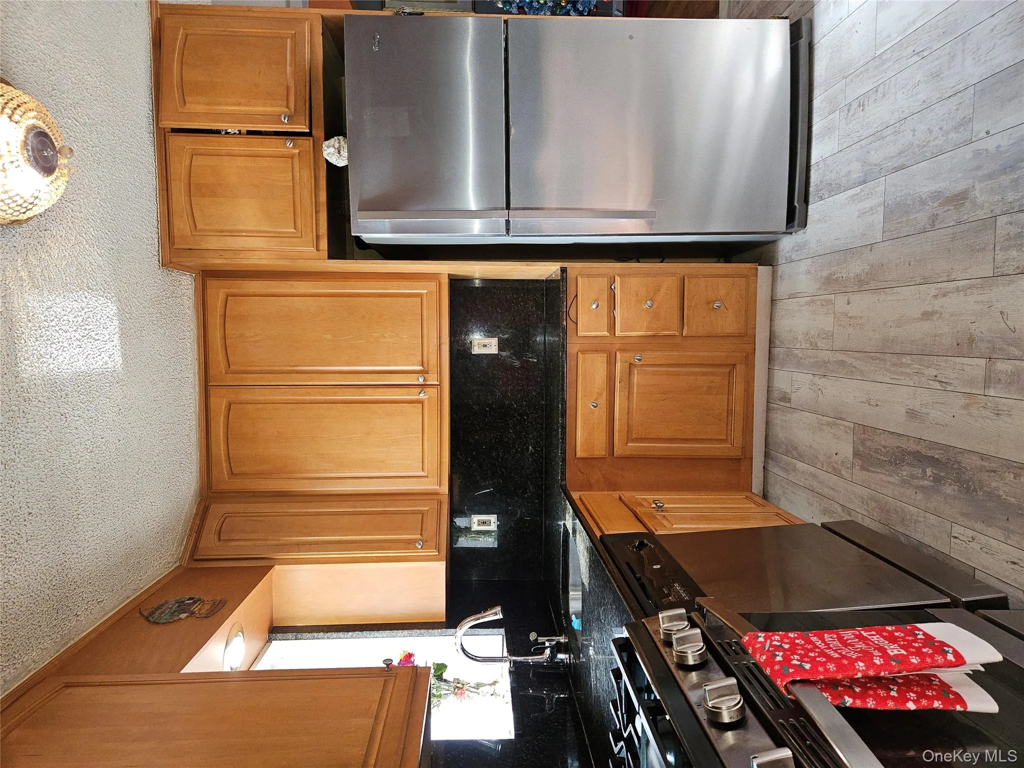 Kitchen featuring stainless steel fridge, range, brown cabinetry, dark stone countertops, and a textured ceiling Kitchen featuring stainless steel fridge, range, brown cabinetry, dark stone countertops, and a textured ceiling