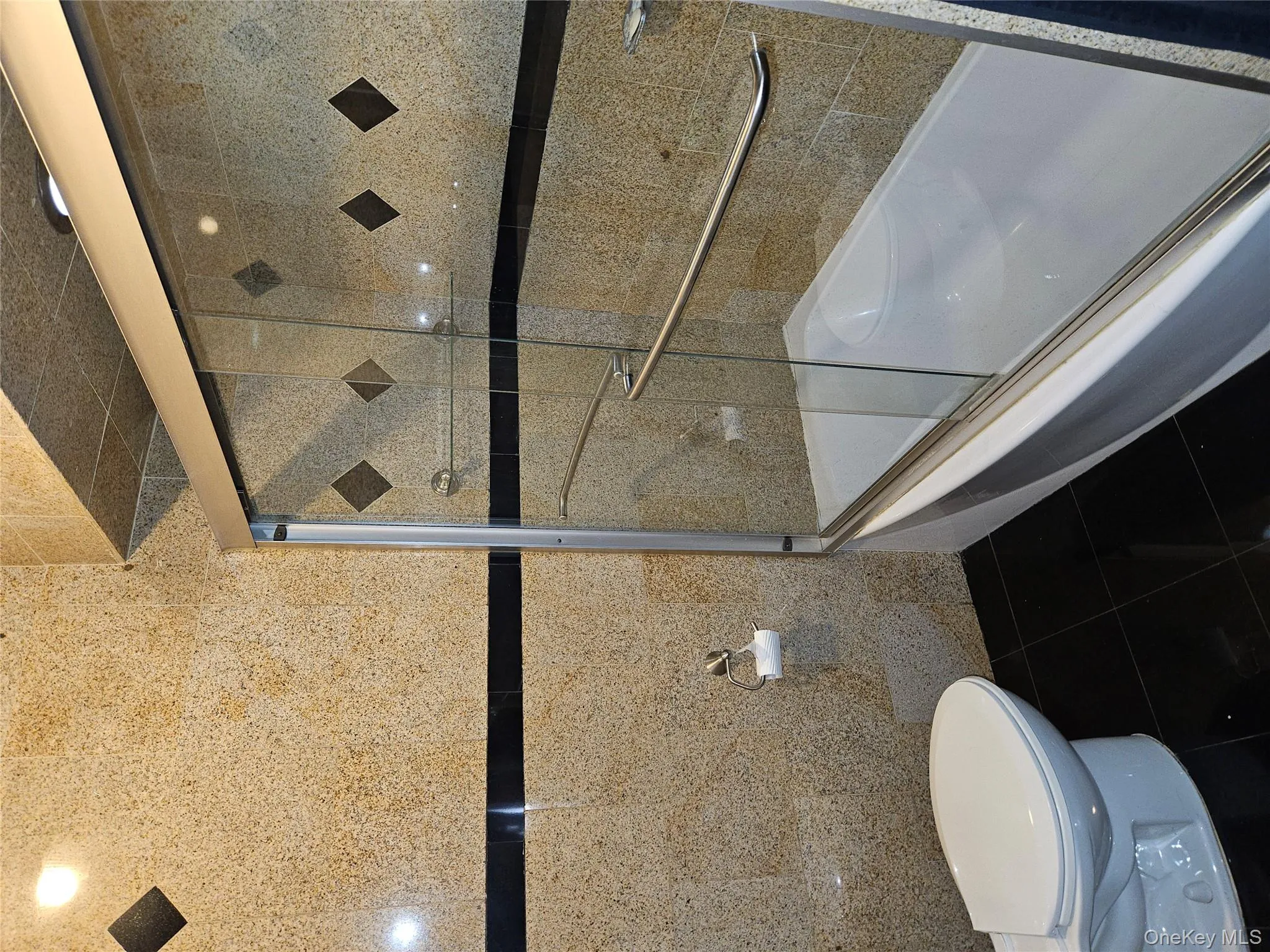 Bathroom with tile walls, shower / bath combination with glass door, and dark tile patterned flooring Bathroom with tile walls, shower / bath combination with glass door, and dark tile patterned flooring