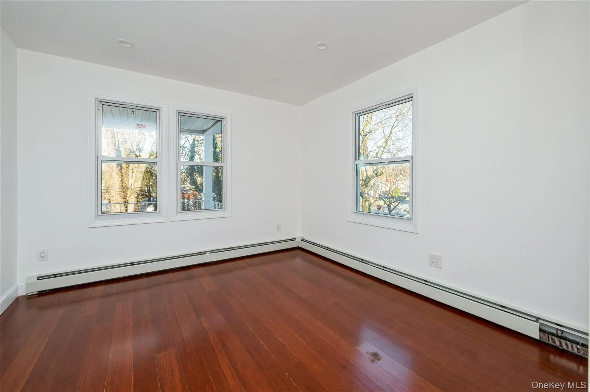 Unfurnished room with a baseboard heating unit, dark wood-type flooring, and plenty of natural light Unfurnished room with a baseboard heating unit, dark wood-type flooring, and plenty of natural light