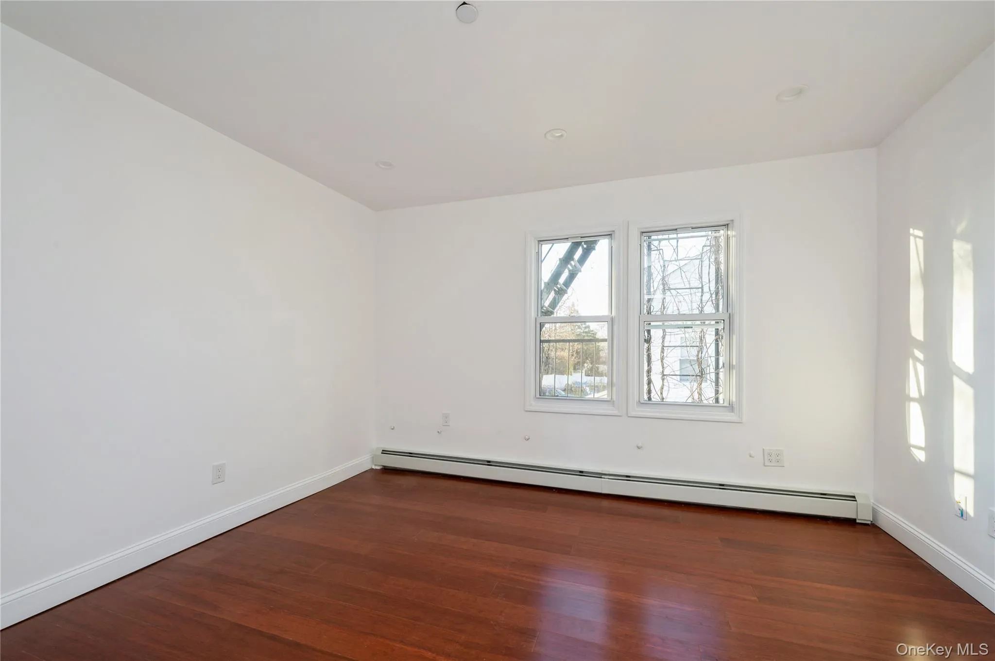 Spare room with a baseboard radiator and dark wood-style floors Spare room with a baseboard radiator and dark wood-style floors
