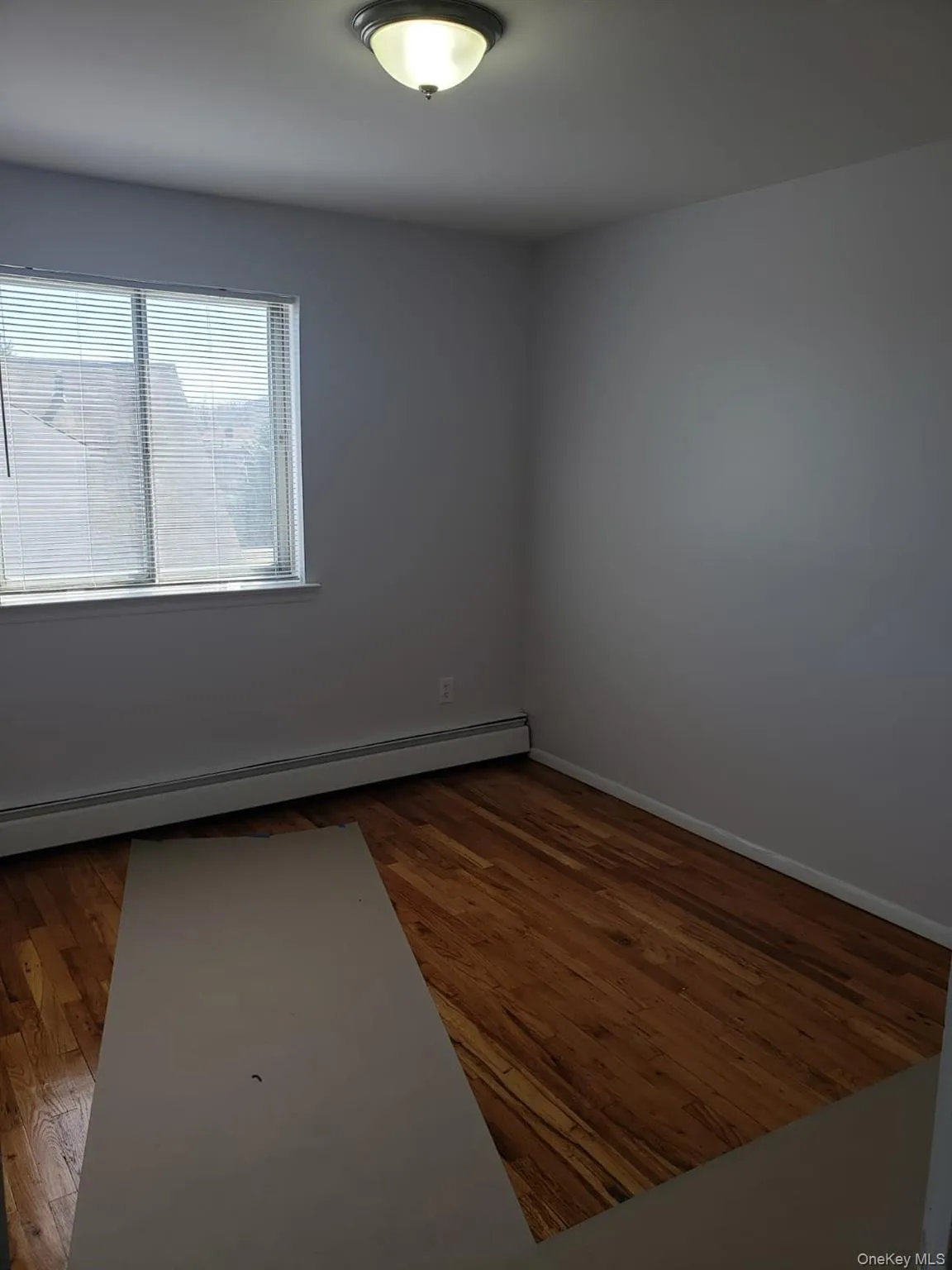 Unfurnished room with baseboard heating and dark wood-style floors Unfurnished room with baseboard heating and dark wood-style floors