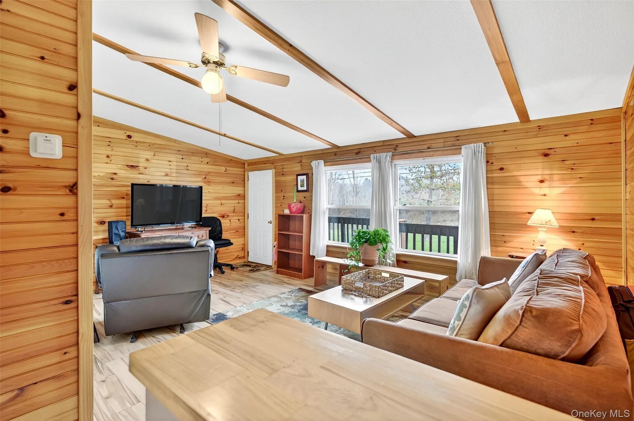 Living room with vaulted ceiling, wooden walls, ceiling fan, wood finished floors, and an office area Living room with vaulted ceiling, wooden walls, ceiling fan, wood finished floors, and an office area