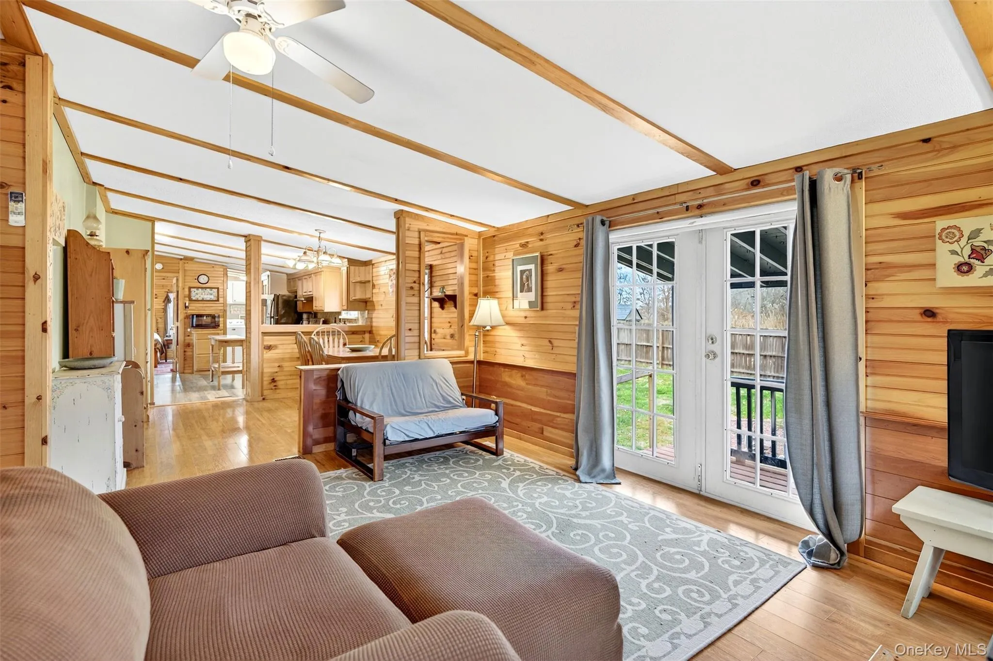 Living area featuring wooden walls, light wood finished floors, french doors, a ceiling fan, and beam ceiling Living area featuring wooden walls, light wood finished floors, french doors, a ceiling fan, and beam ceiling