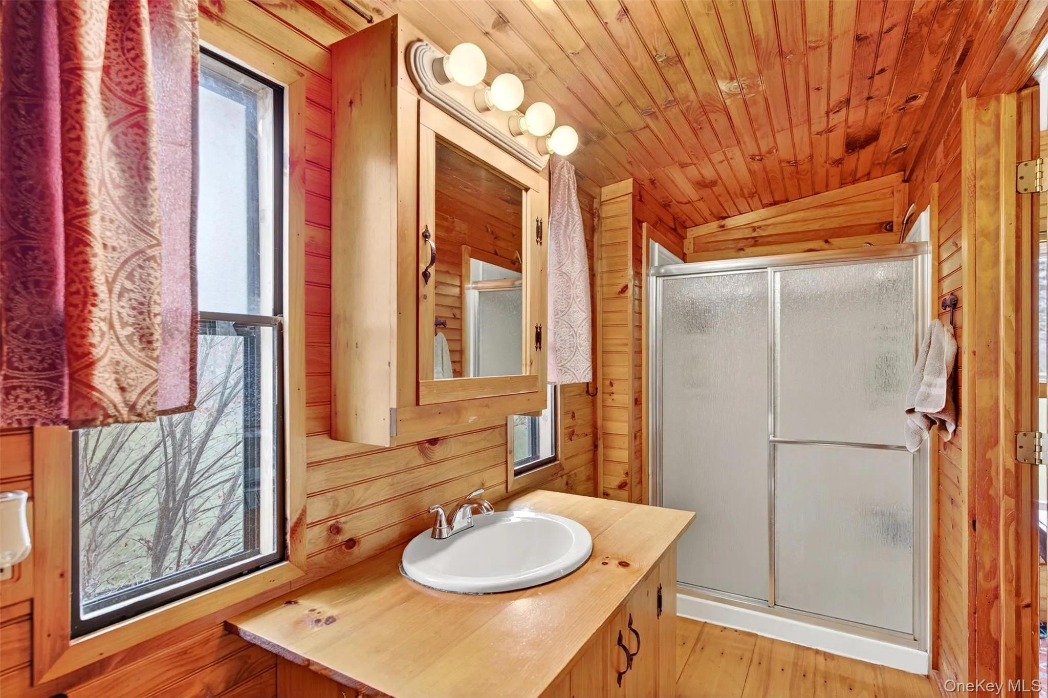 Full bath with wood walls, vanity, vaulted ceiling, a shower stall, and wood ceiling Full bath with wood walls, vanity, vaulted ceiling, a shower stall, and wood ceiling