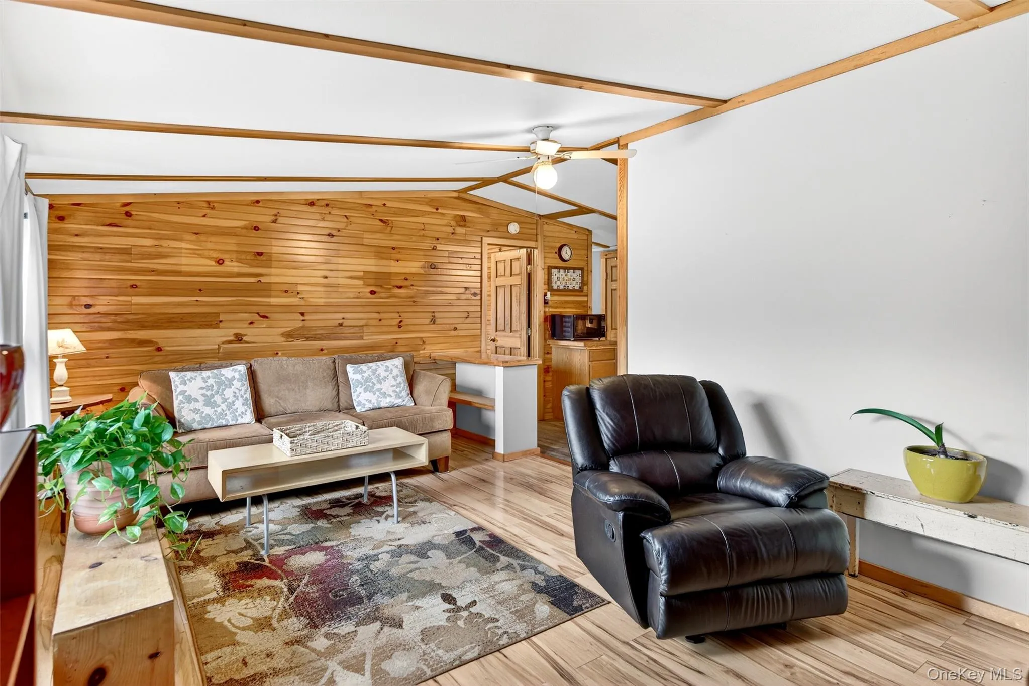 Living room featuring wooden walls, vaulted ceiling, ceiling fan, and light wood-style floors Living room featuring wooden walls, vaulted ceiling, ceiling fan, and light wood-style floors