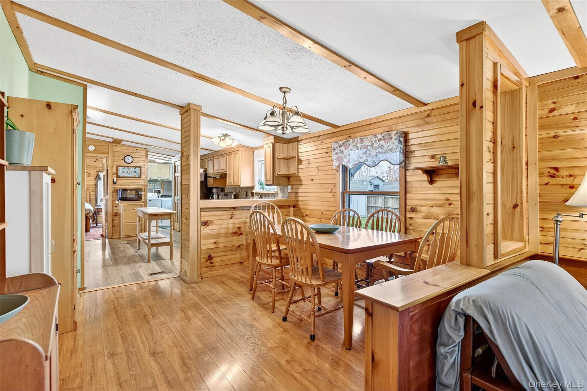 Dining room with wood walls, beamed ceiling, light wood-style floors, a textured ceiling, and a chandelier Dining room with wood walls, beamed ceiling, light wood-style floors, a textured ceiling, and a chandelier