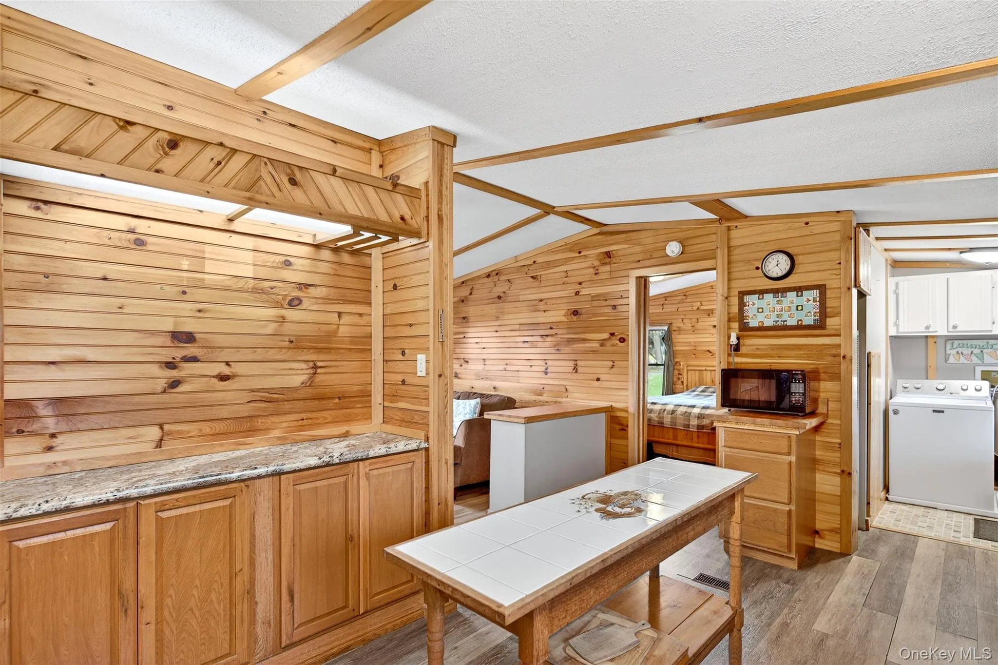 Kitchen with wood walls, washer / dryer, light wood-type flooring, black microwave, and brown cabinetry Kitchen with wood walls, washer / dryer, light wood-type flooring, black microwave, and brown cabinetry